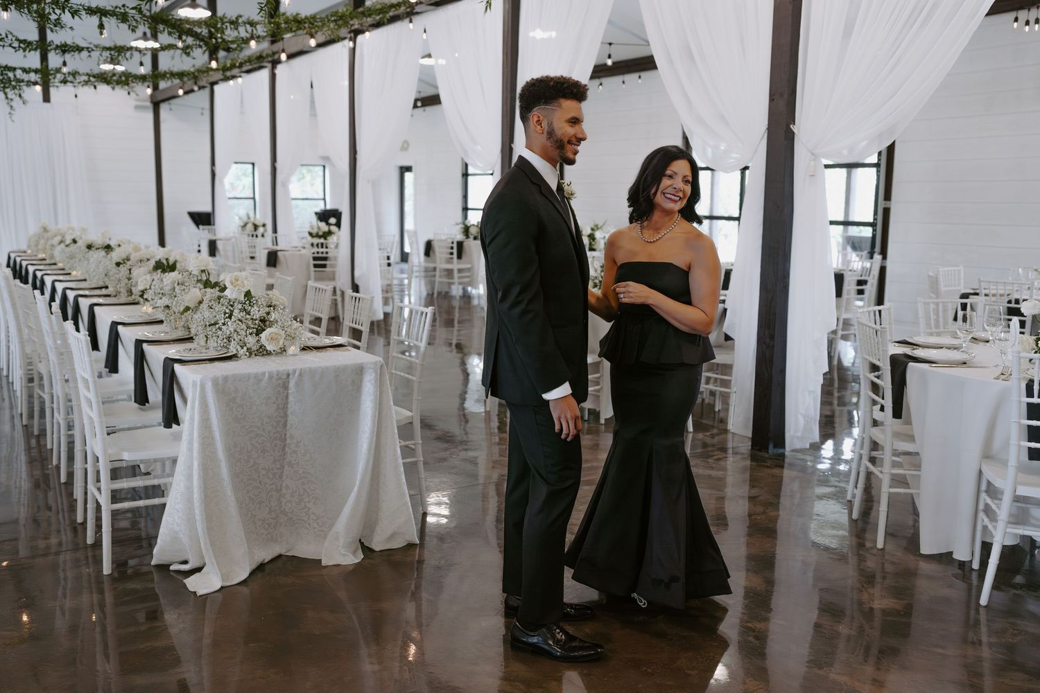 A modern reception venue featuring white drapes, elegant lighting and polished wooden floors.