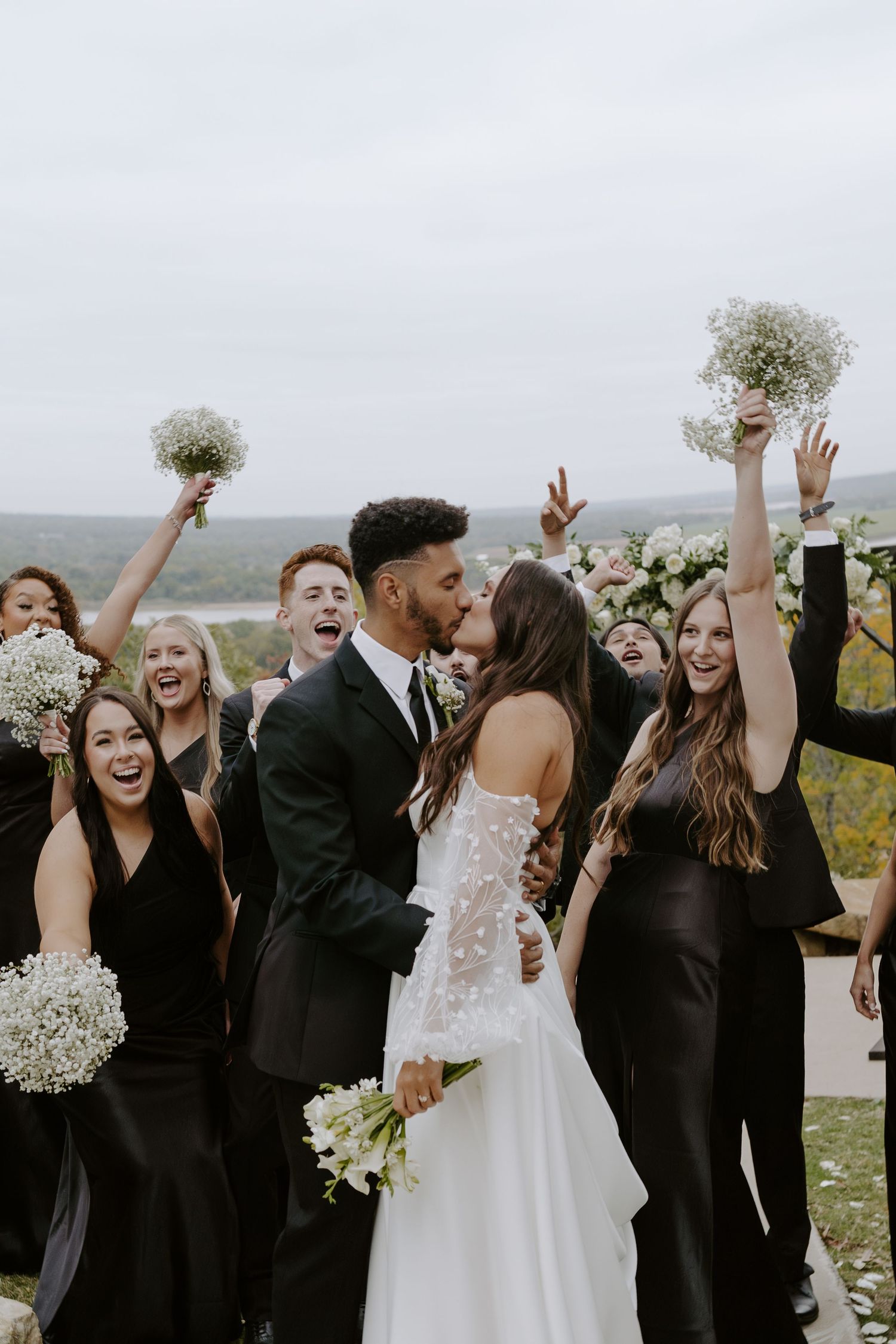 Wedding celebration with joyful group wearing black and white attire cheering outdoors.