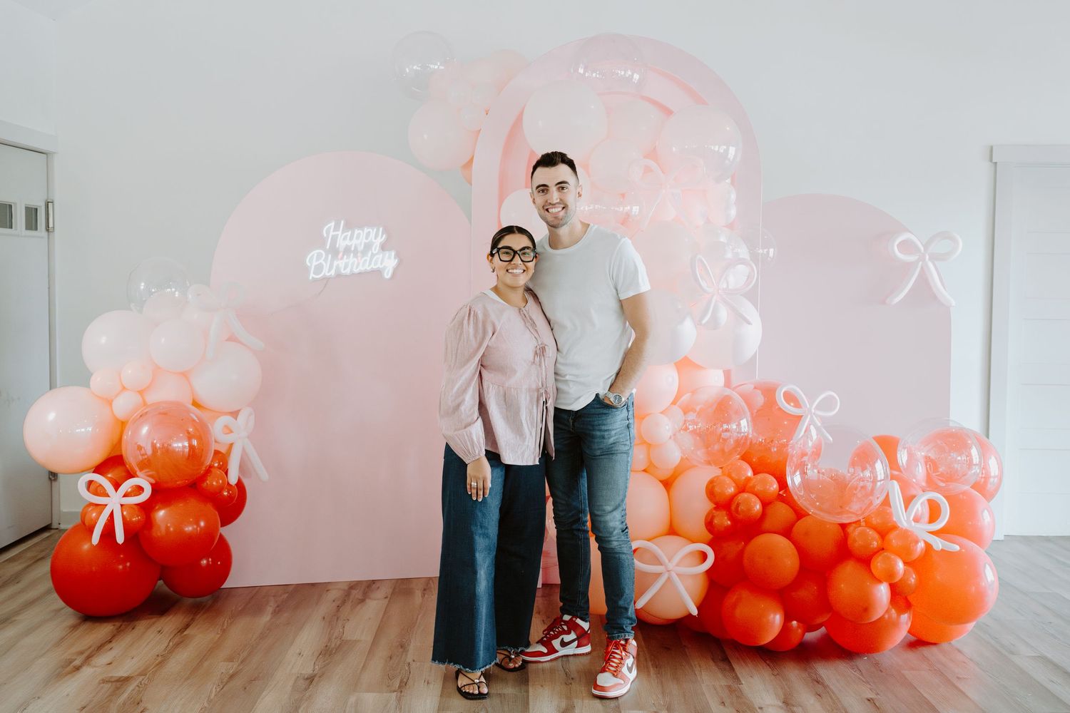 Pink and orange balloon decorations create a festive backdrop against a white wall.