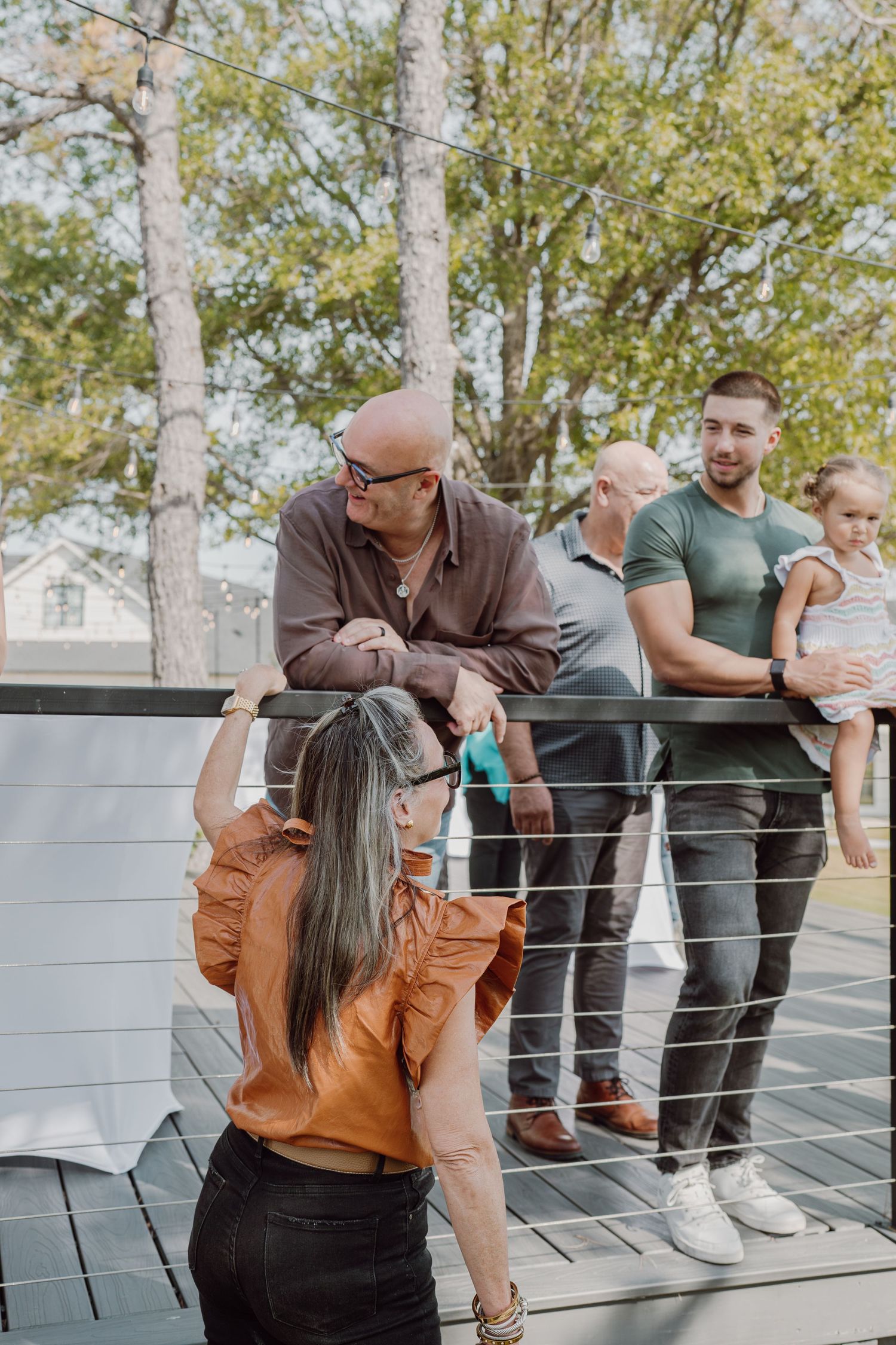 People gather on a modern deck with metal railings during an outdoor event.