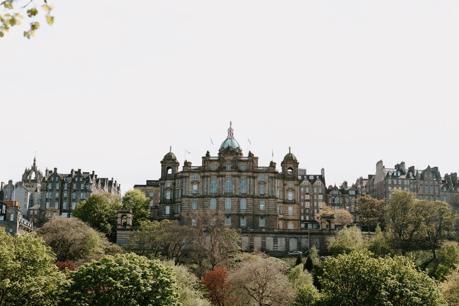 Historic Edinburgh cityscape with grand Victorian buildings and architecture against cloudy sky.