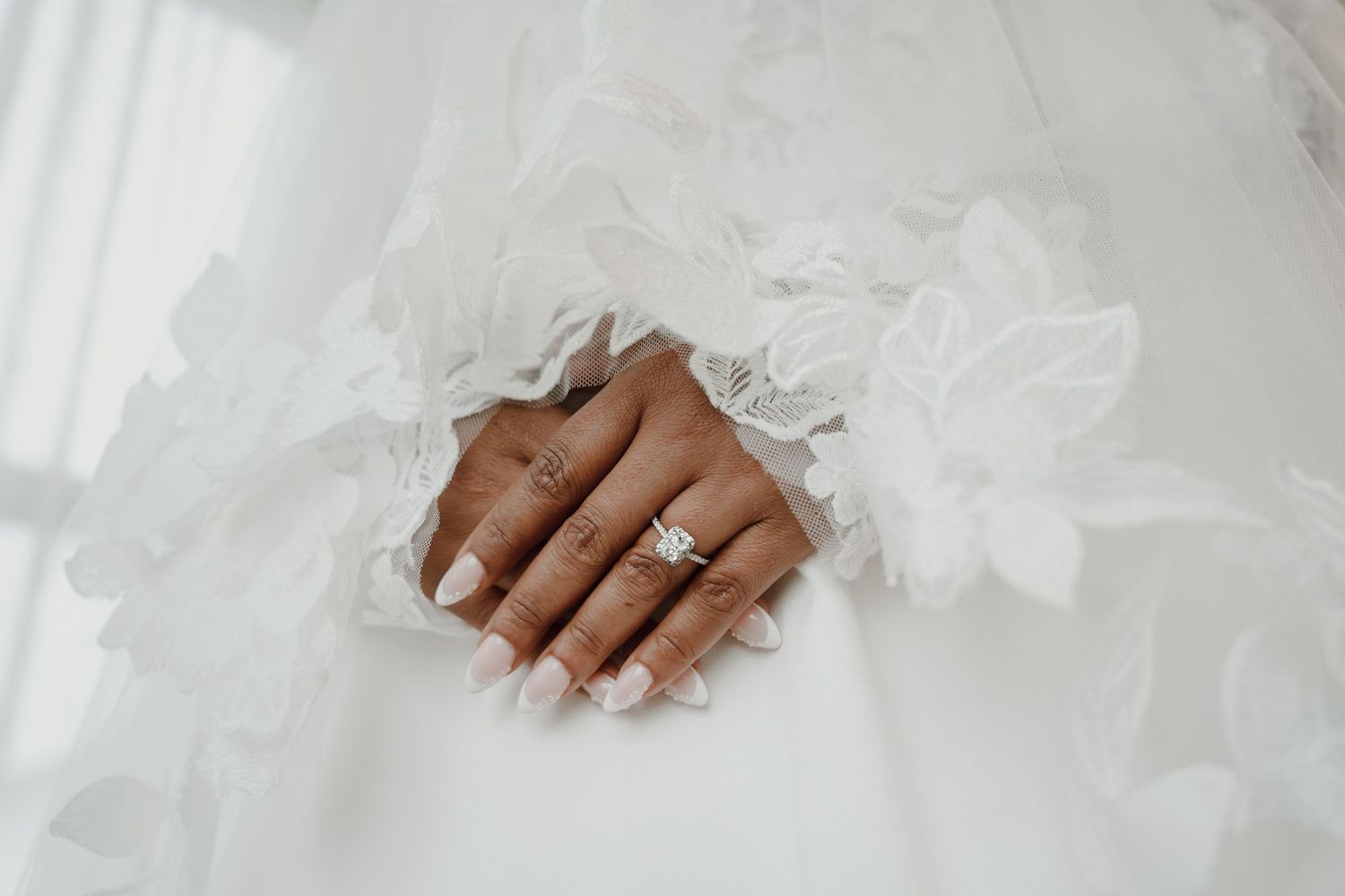Close-up detail of bridal hands with engagement ring and lace dress details.