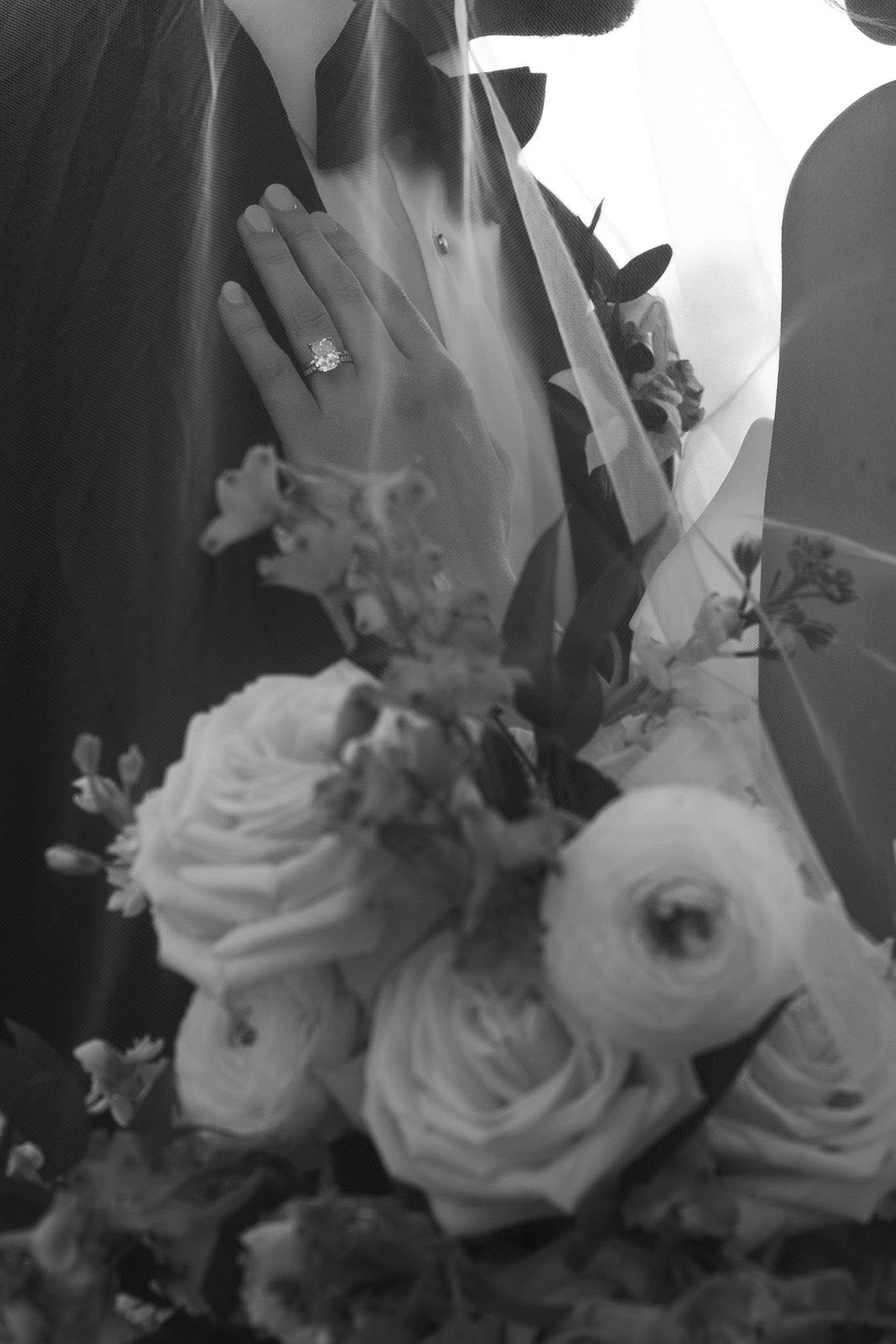 Black and white photo of a bride holding a floral bouquet with roses, showcasing an elegant diamond engagement ring.