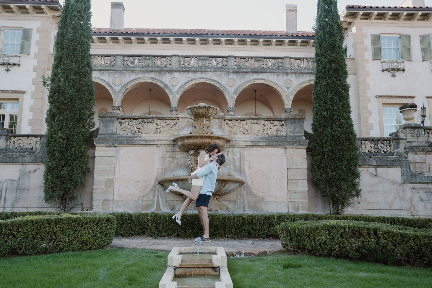 A romantic scene in front of an ornate Italian villa with cypress trees and classical architecture.