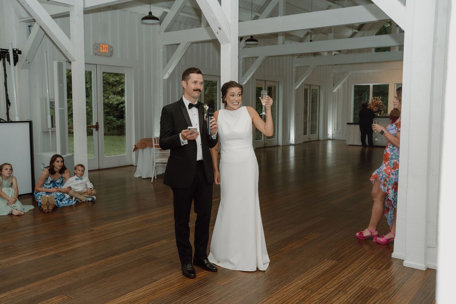 Couple raising their glasses in celebration at a bright white barn wedding venue.