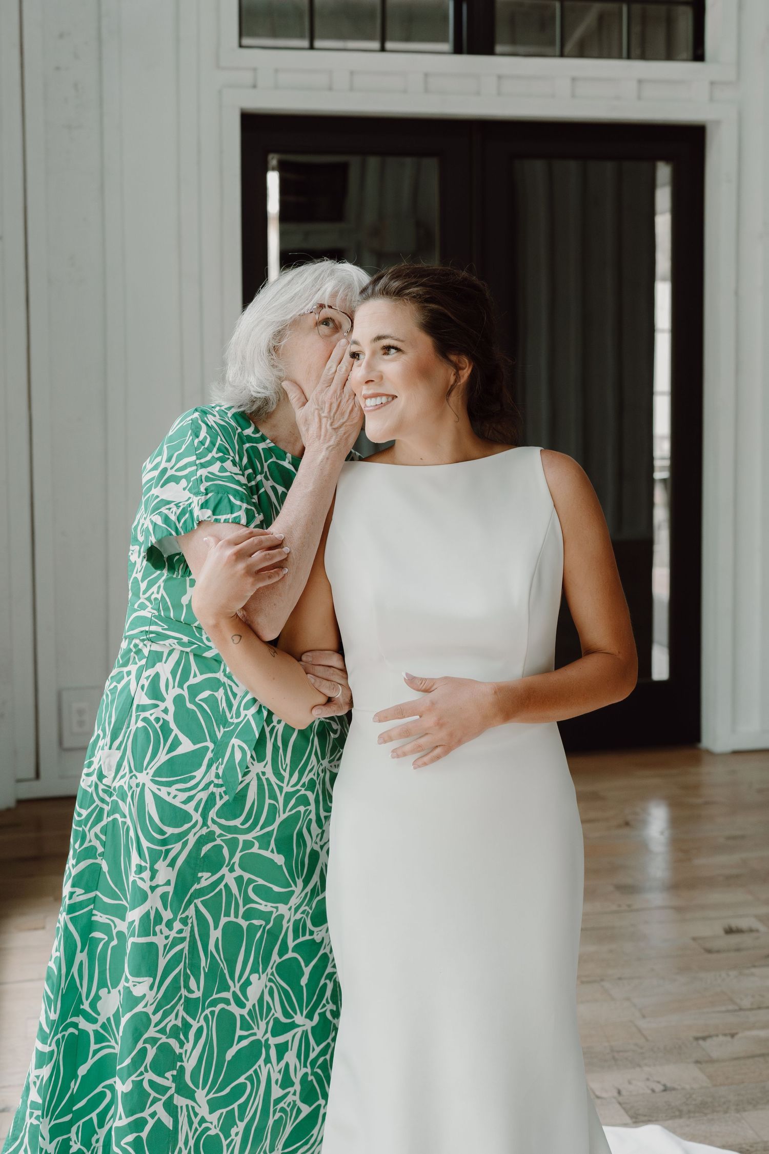 Emotional wedding day moment captured between two people embracing in white and green dresses.
