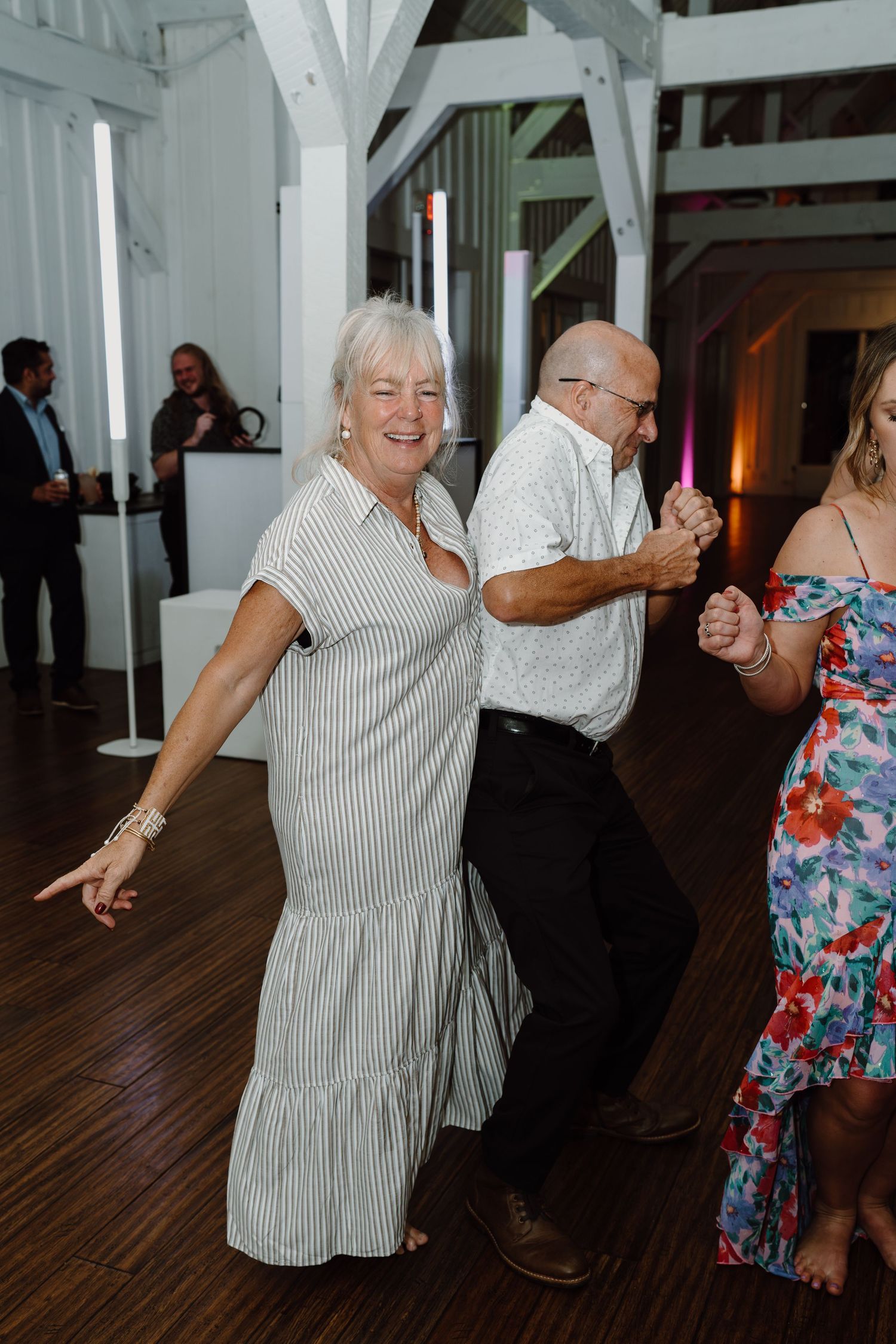 Wedding guests dancing and celebrating on a wooden dance floor with white beamed walls.