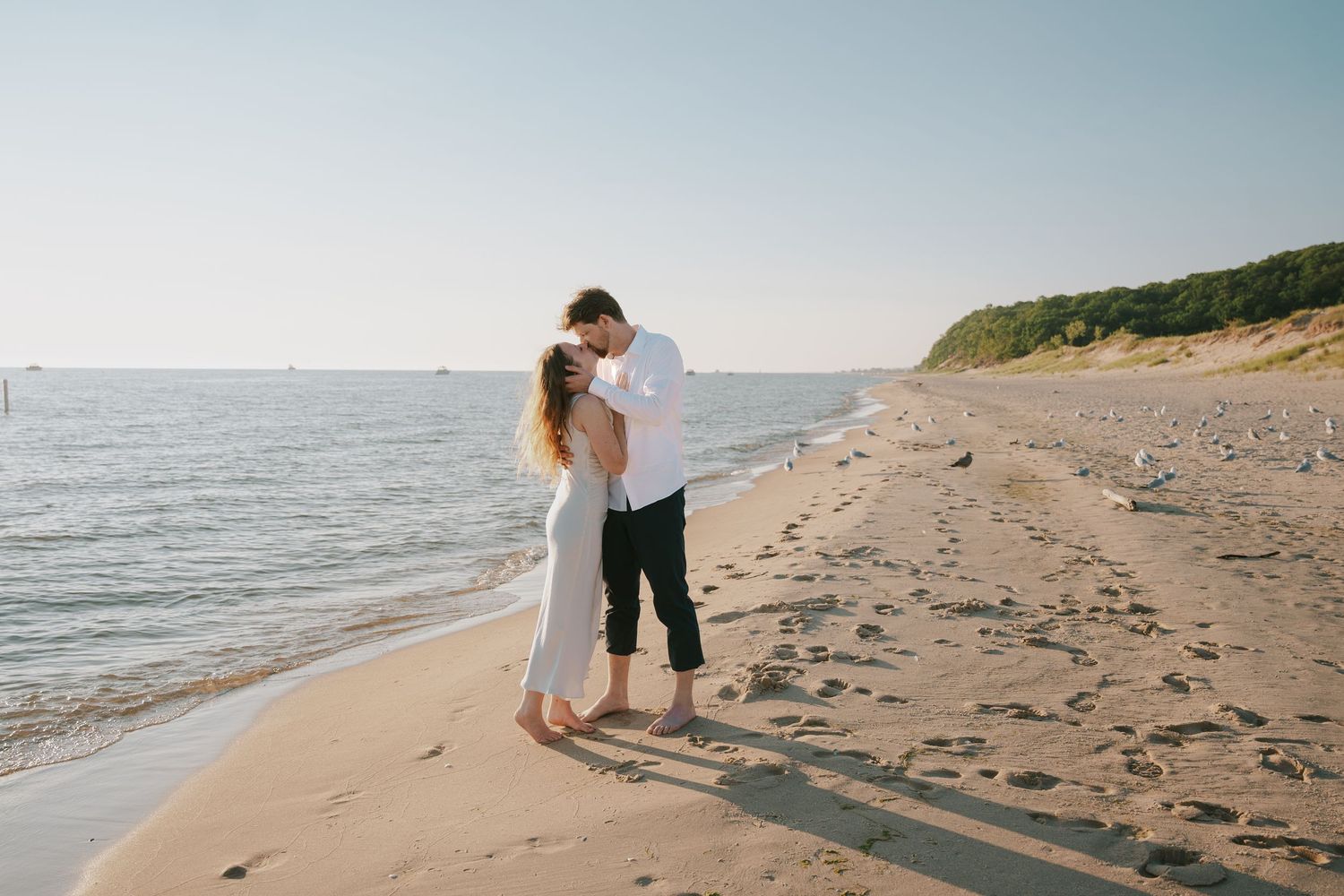 Couple shares tender moment on secluded beach with cliffs in the distance.
