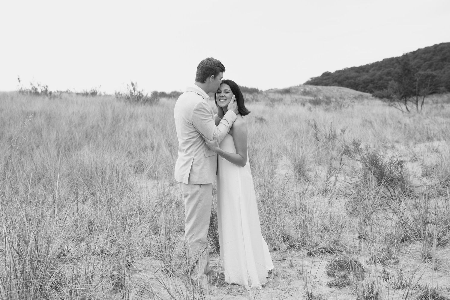 Black and white wedding portrait showing a tender moment between a couple on sandy dunes.