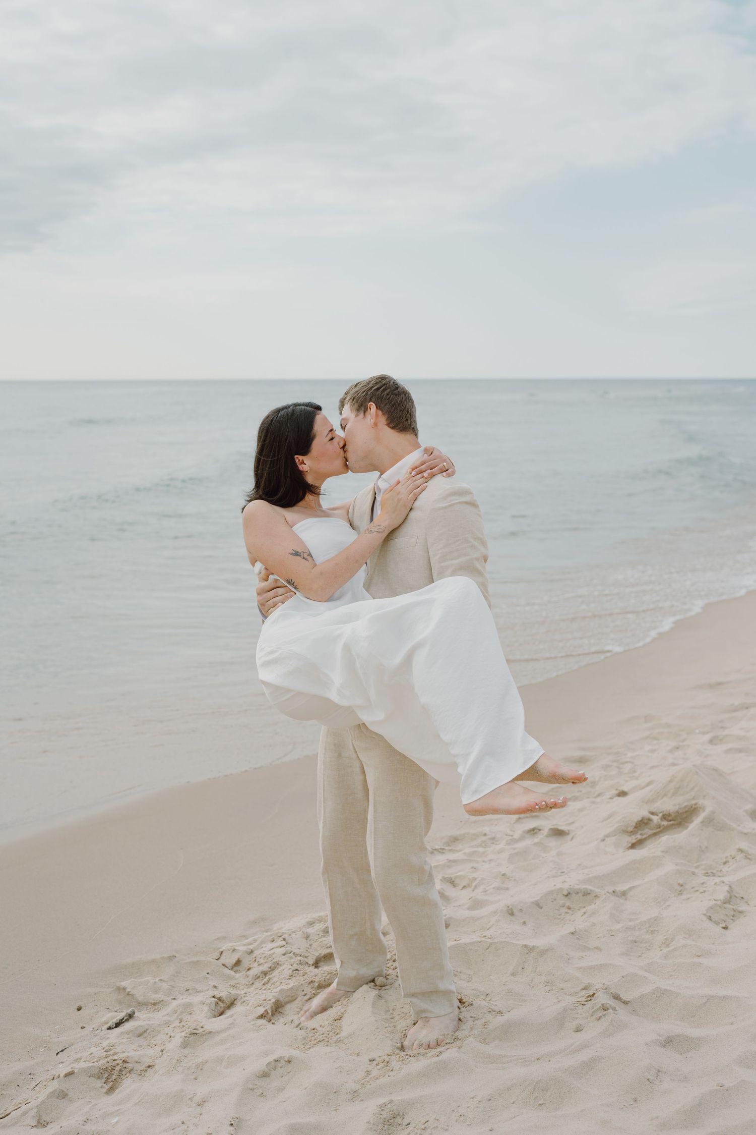 Couple shares intimate moment while dancing on beach with waves and cloudy sky in background.