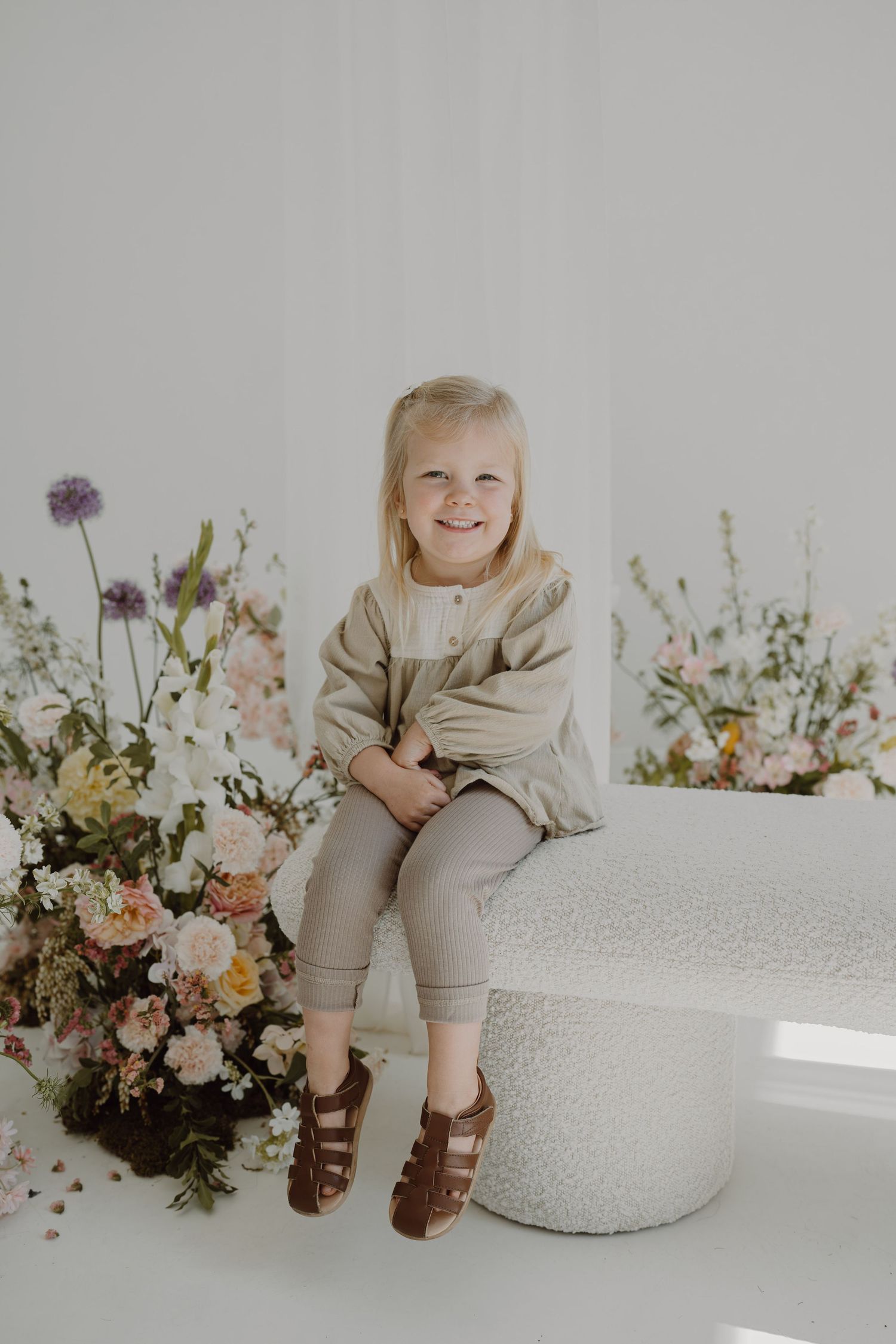 White studio setting with textured round ottoman and romantic floral arrangements in soft lighting.