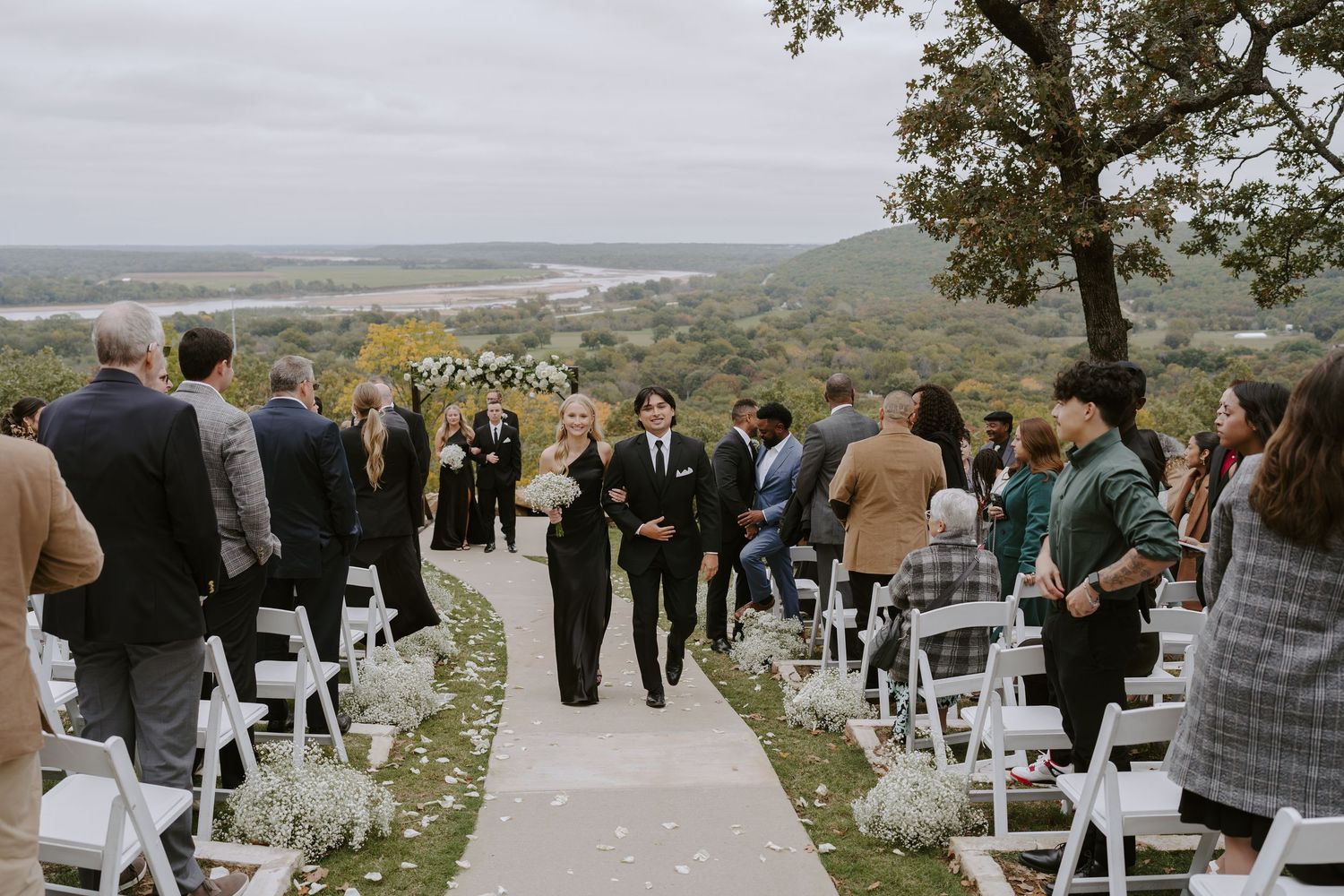 Guests mingle before a wedding ceremony on a scenic overlook with white chairs and mountain views.