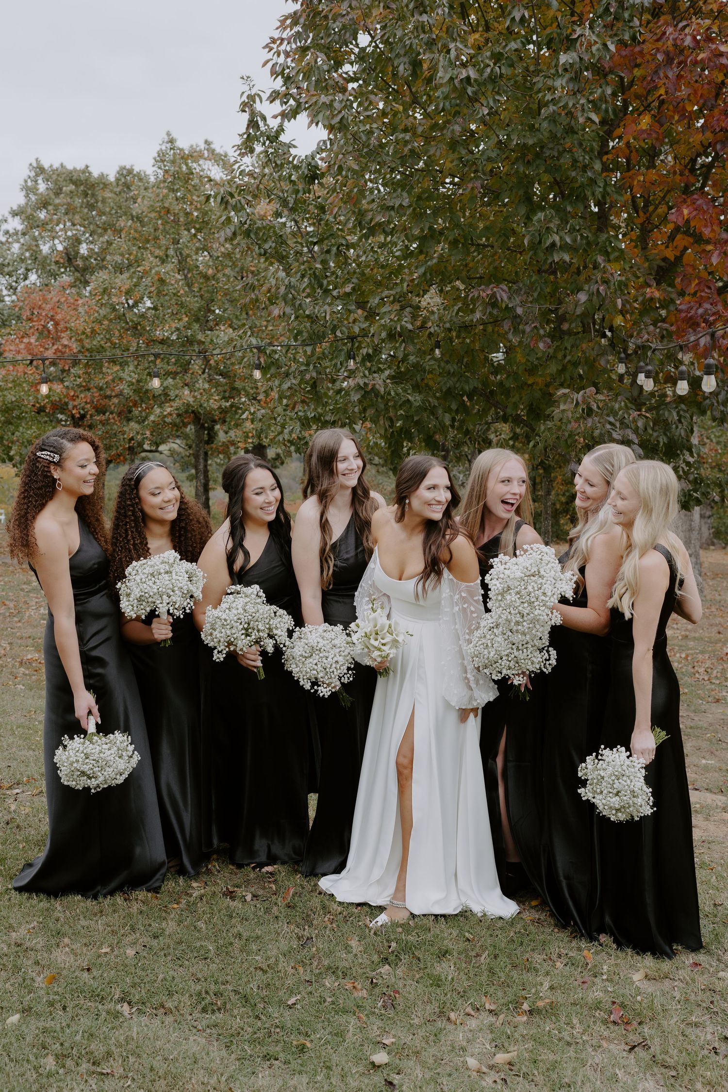Wedding party in black bridesmaid dresses and white gowns pose together outdoors during autumn.