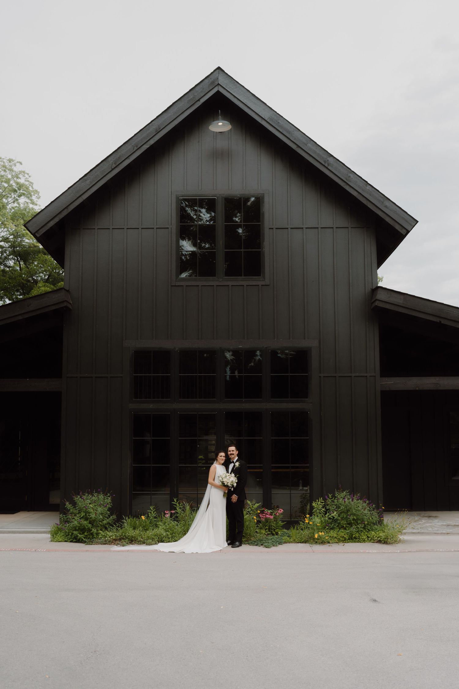 Modern black barn-style wedding venue with large windows and minimalist architecture set against a natural landscape.
