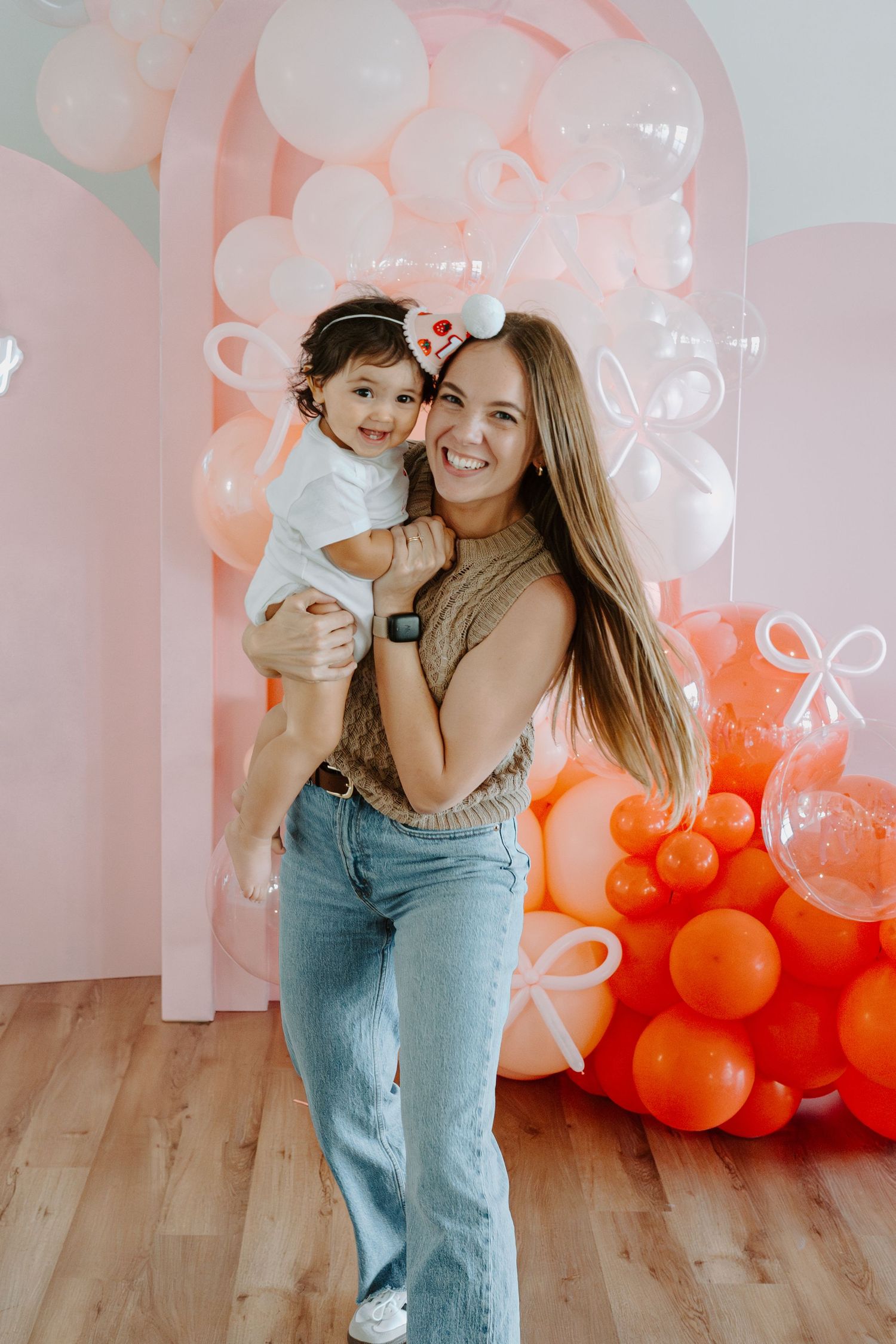 Joyful moment captured in front of a decorative balloon display in warm peach tones.