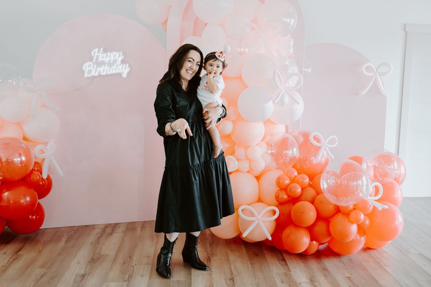 Birthday celebration backdrop featuring elegant coral and white balloon arrangement with decorative bows.