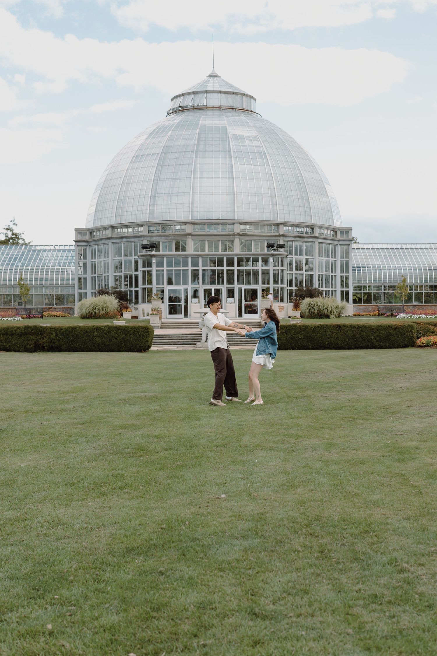 Couple dancing on manicured lawn with iconic glass domed conservatory building in background.