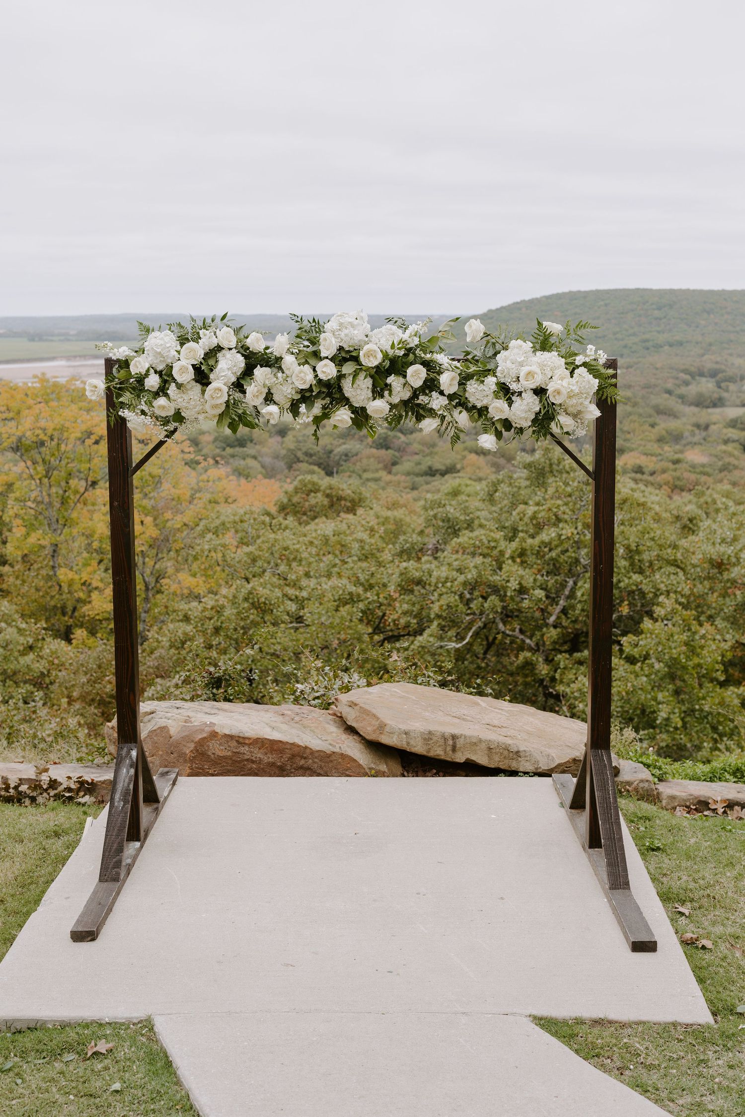 Wedding ceremony altar with wooden posts and white floral arrangements against a scenic hillside backdrop.
