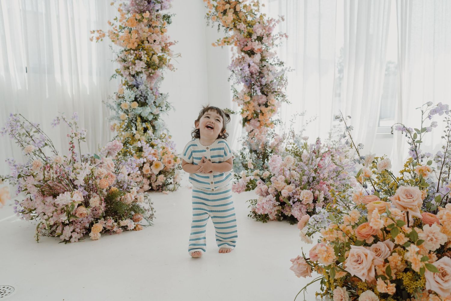 A bright studio setup with delicate floral arrangements in soft pink and peach tones against white curtains.