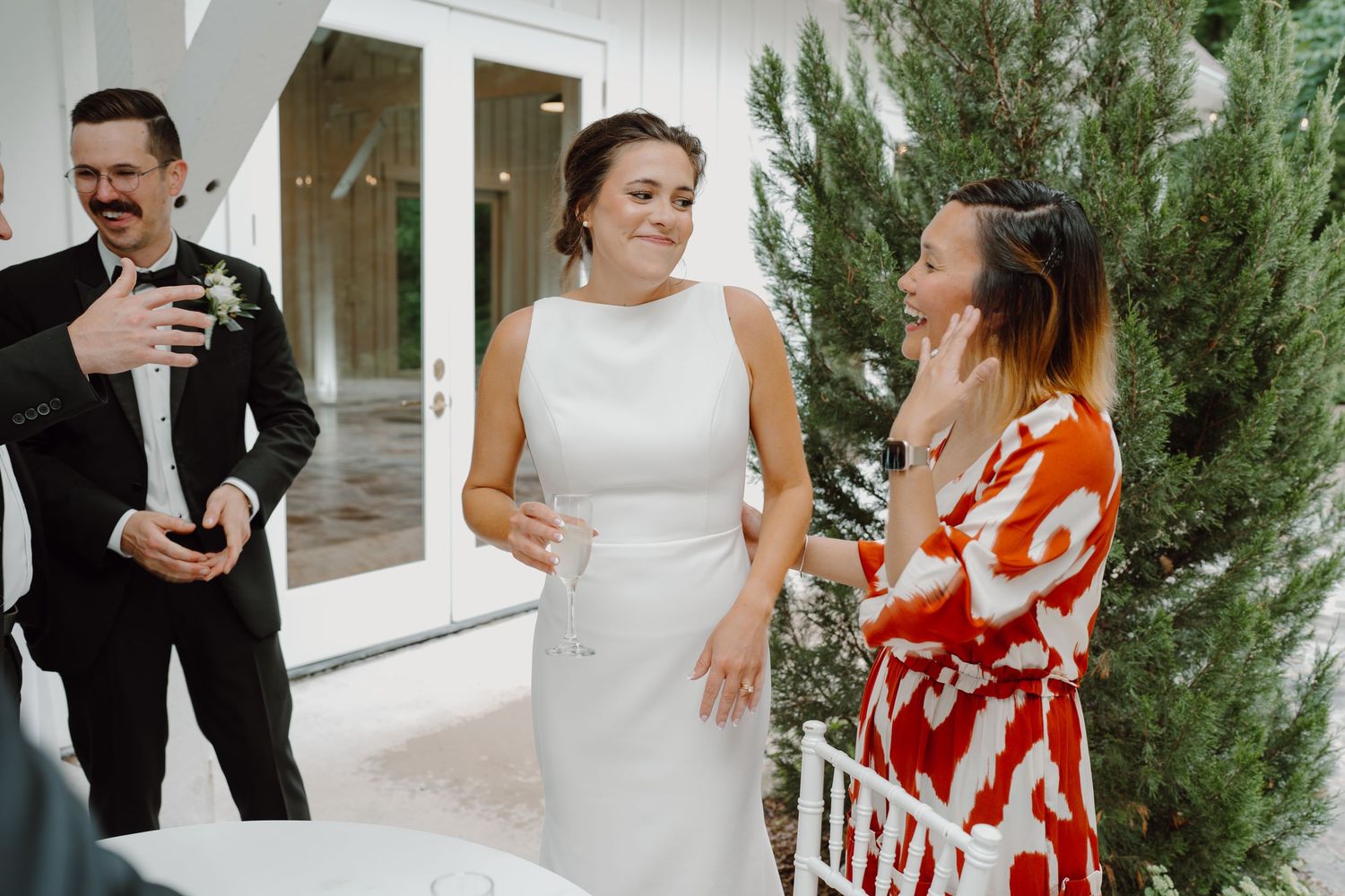 Wedding celebration with guests in formal attire against white walls and evergreen plants.