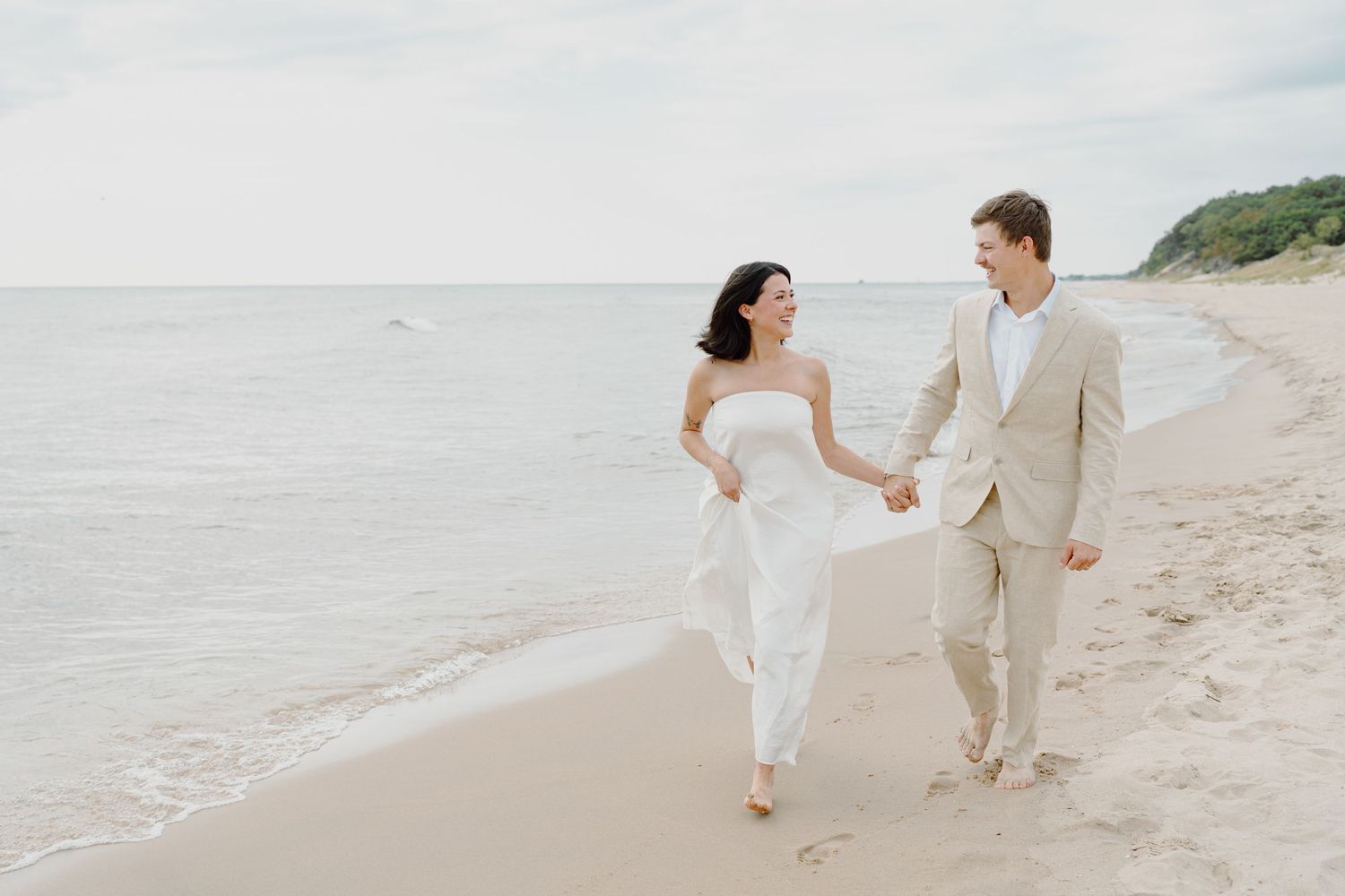 A couple dances and plays together on a serene beach with waves in the background.