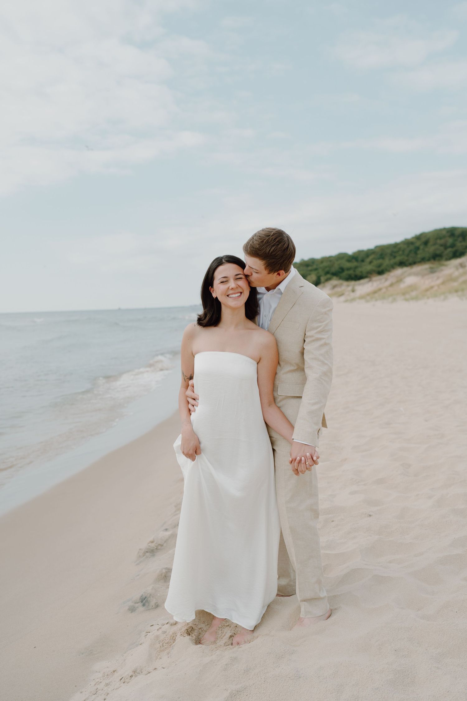 A romantic beach portrait of a couple embracing against a backdrop of blue water and sky.