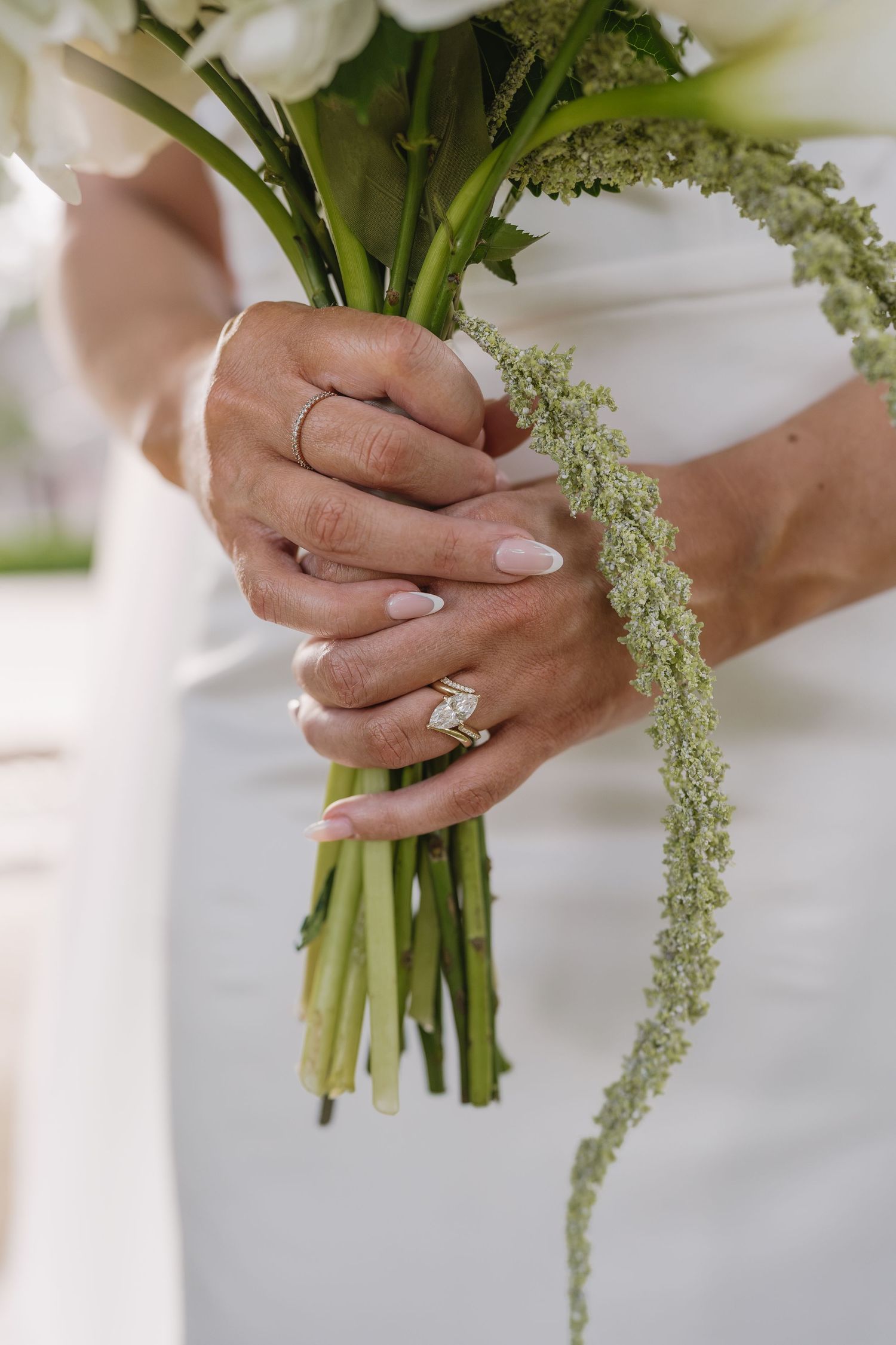 Bride holding a white floral bouquet with trailing greenery, showcasing an elegant diamond engagement ring on her finger.