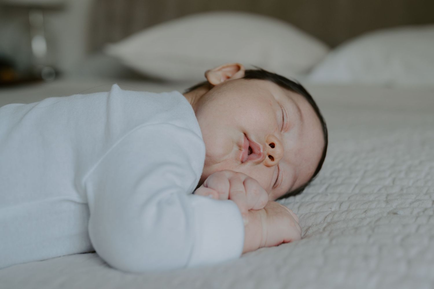 Peaceful newborn baby sleeping in white clothing on soft bedding.