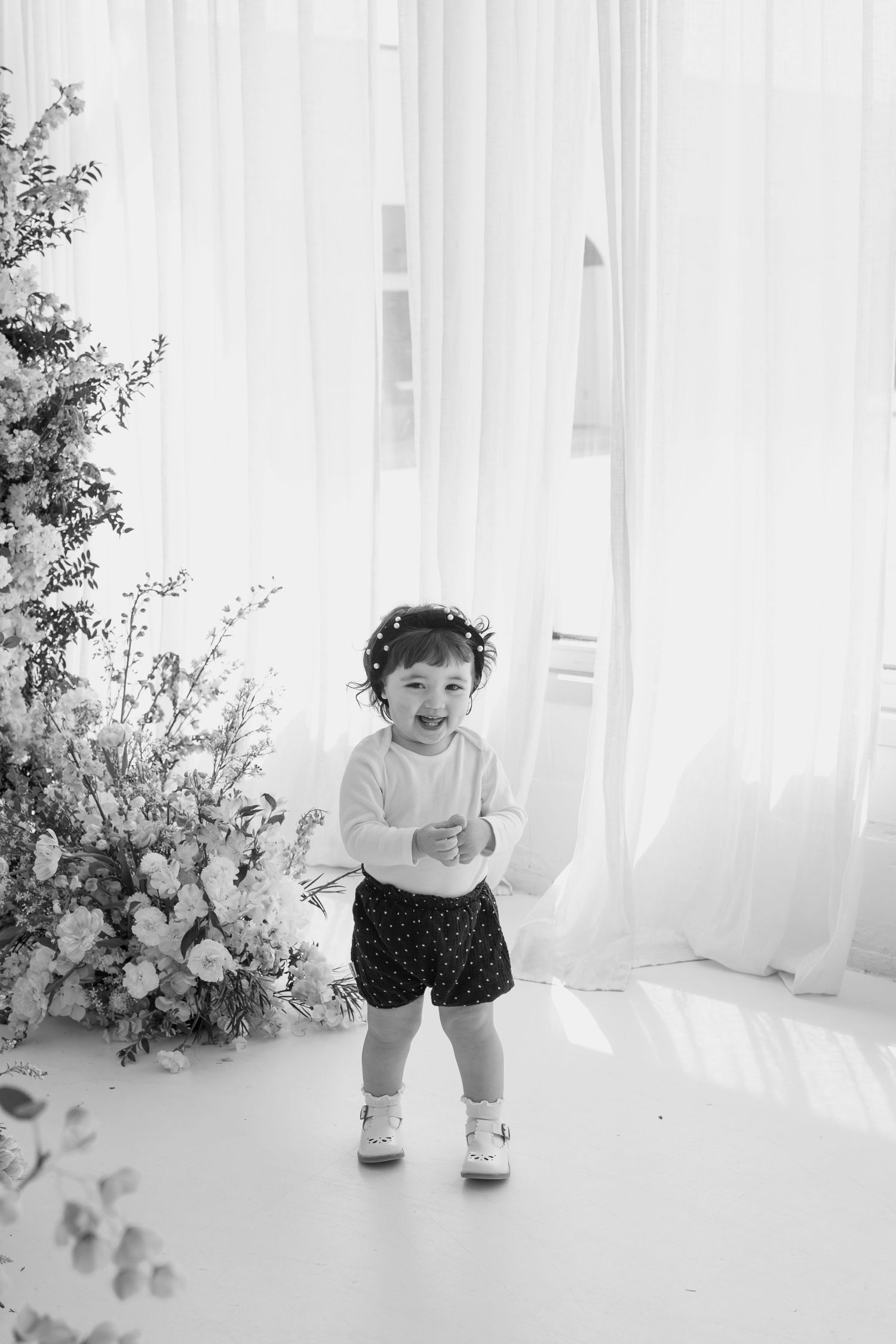Candid black and white portrait of toddler playing in bright studio setting.