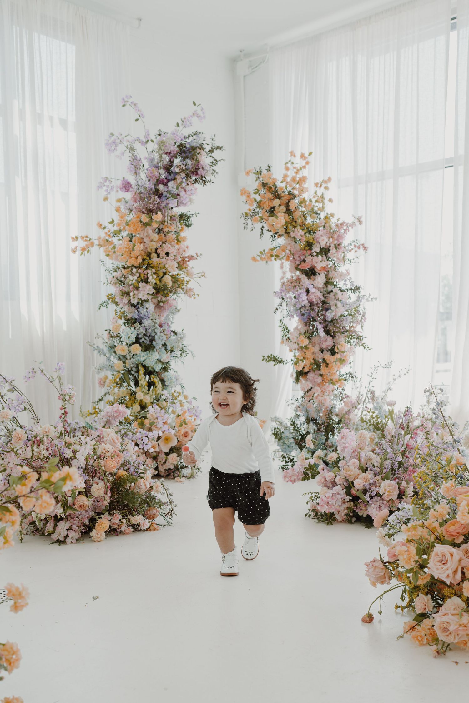Playful scene in a bright white studio with delicate floral arrangements featuring soft pink and peach blooms.