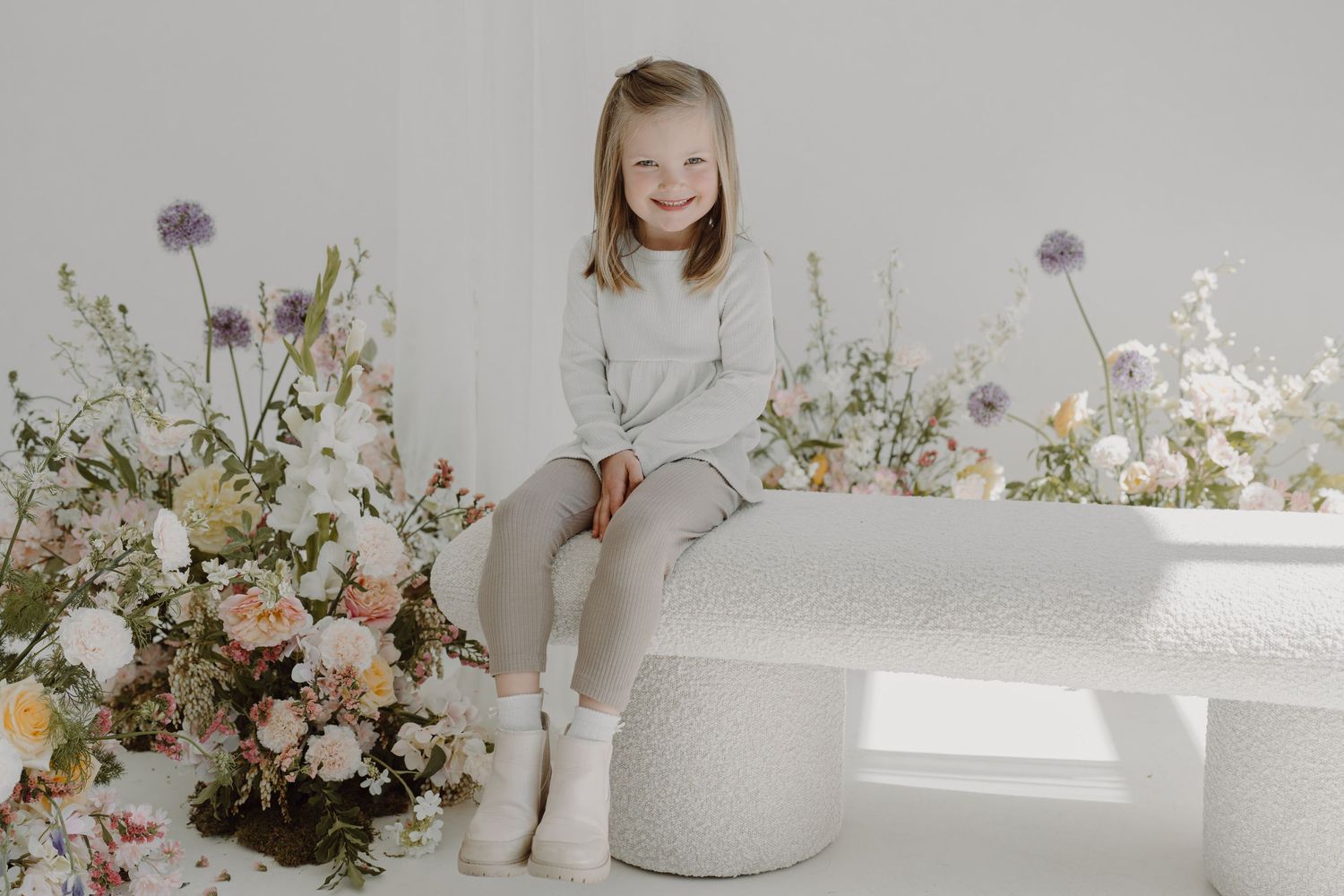 Bright white studio setting with delicate floral arrangements and ceramic vases creating a soft, ethereal atmosphere.