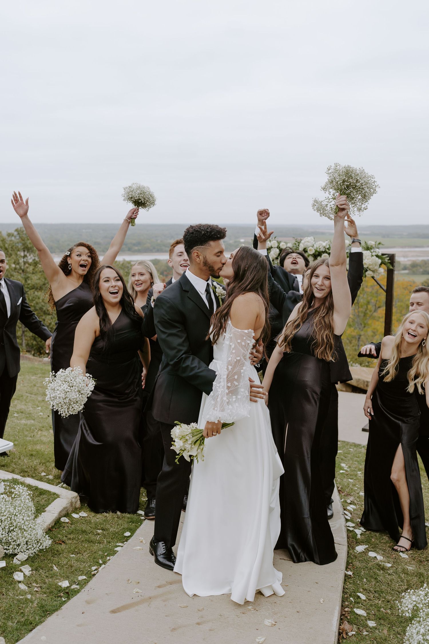 Joyful celebration moment at outdoor wedding with guests cheering on scenic hilltop path.