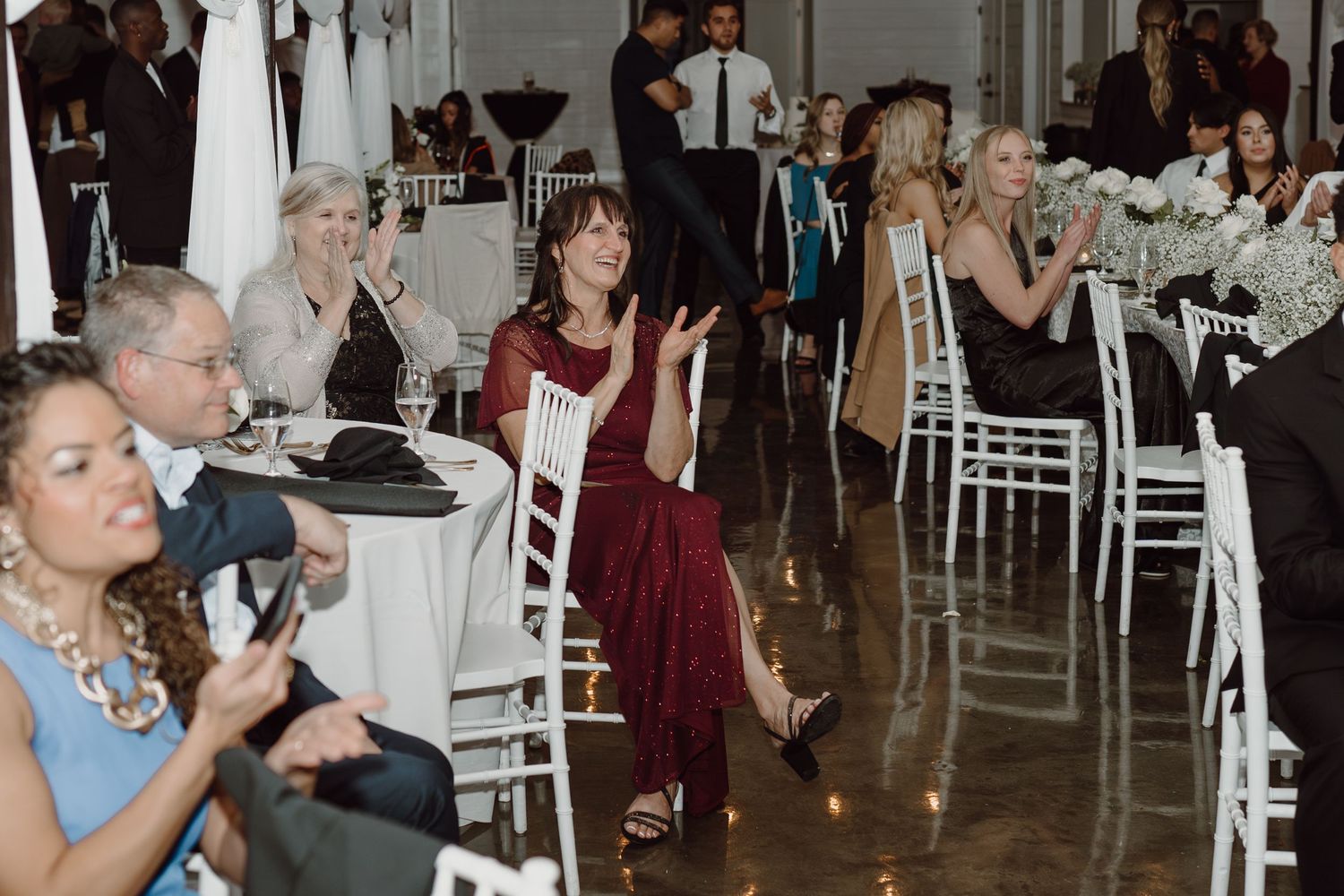 Wedding guests seated at tables with white chairs watch the celebrations unfold.