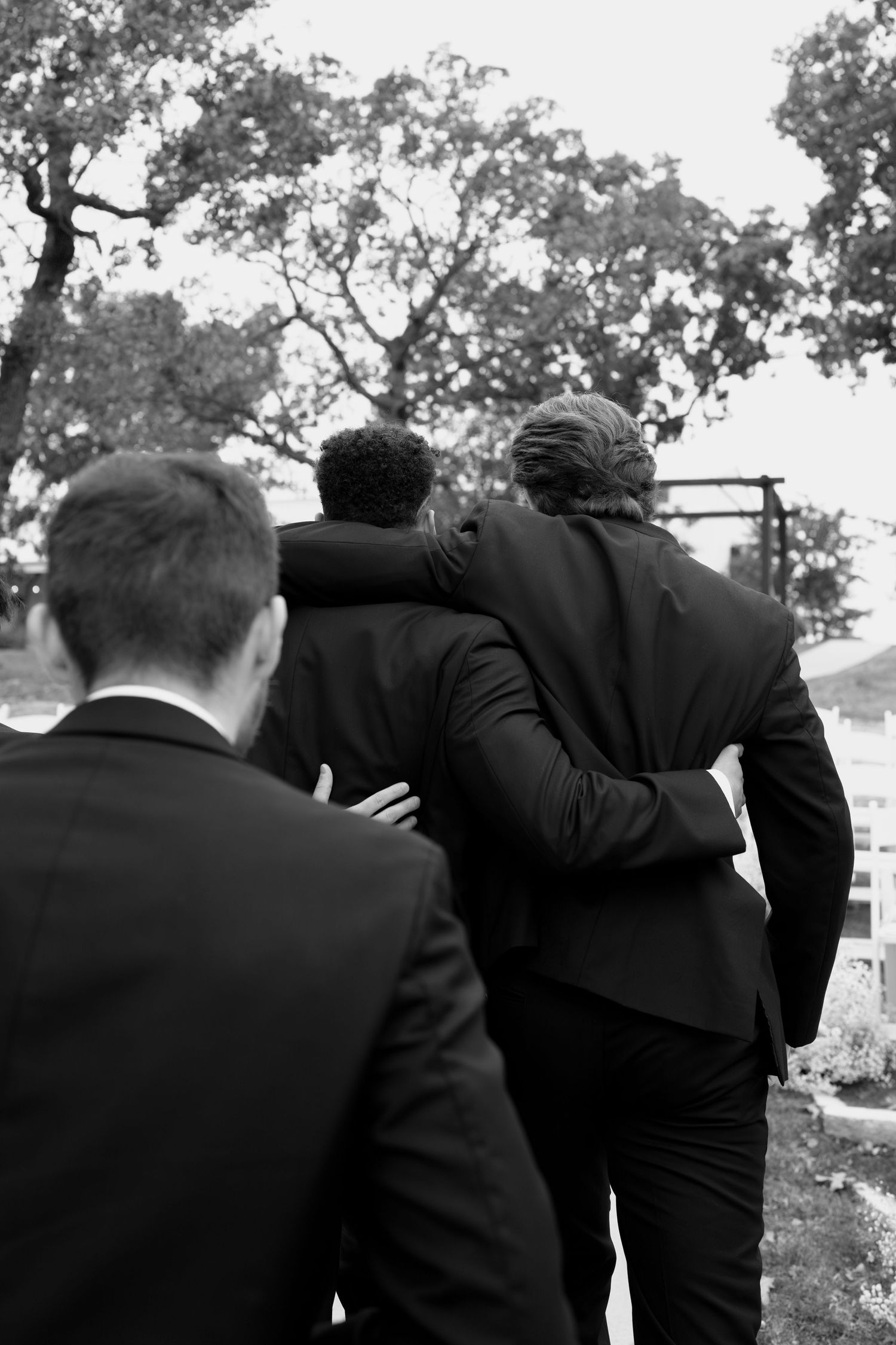 Wedding party members huddle together sharing a group moment outdoors.