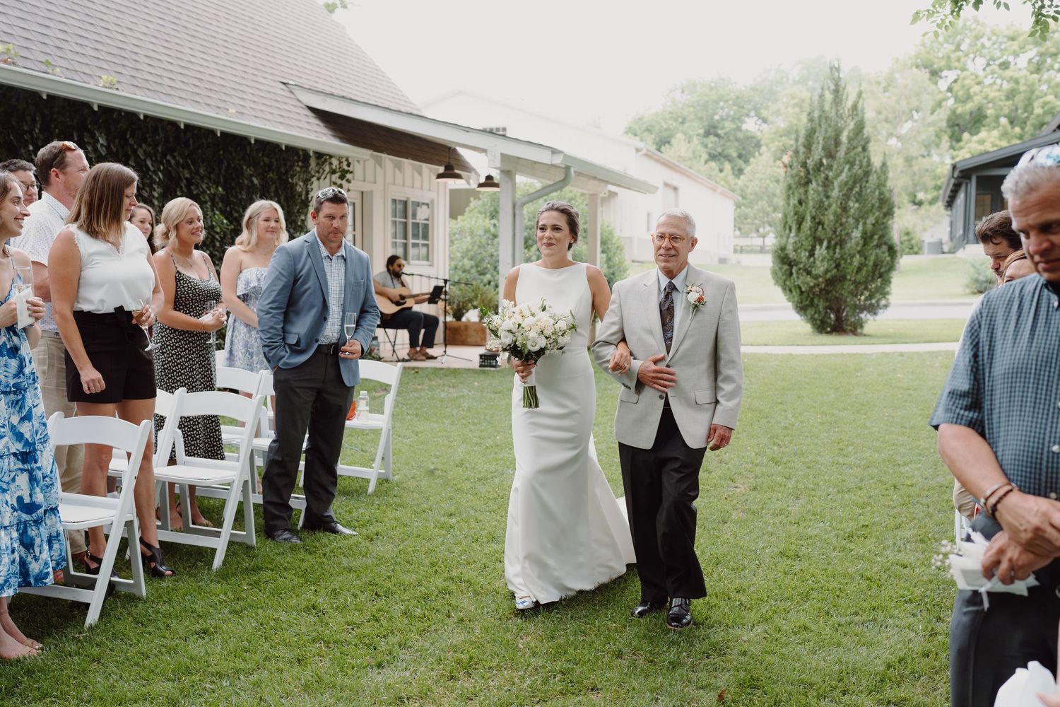 Wedding guests watch as a couple walks down the aisle during an outdoor garden ceremony.