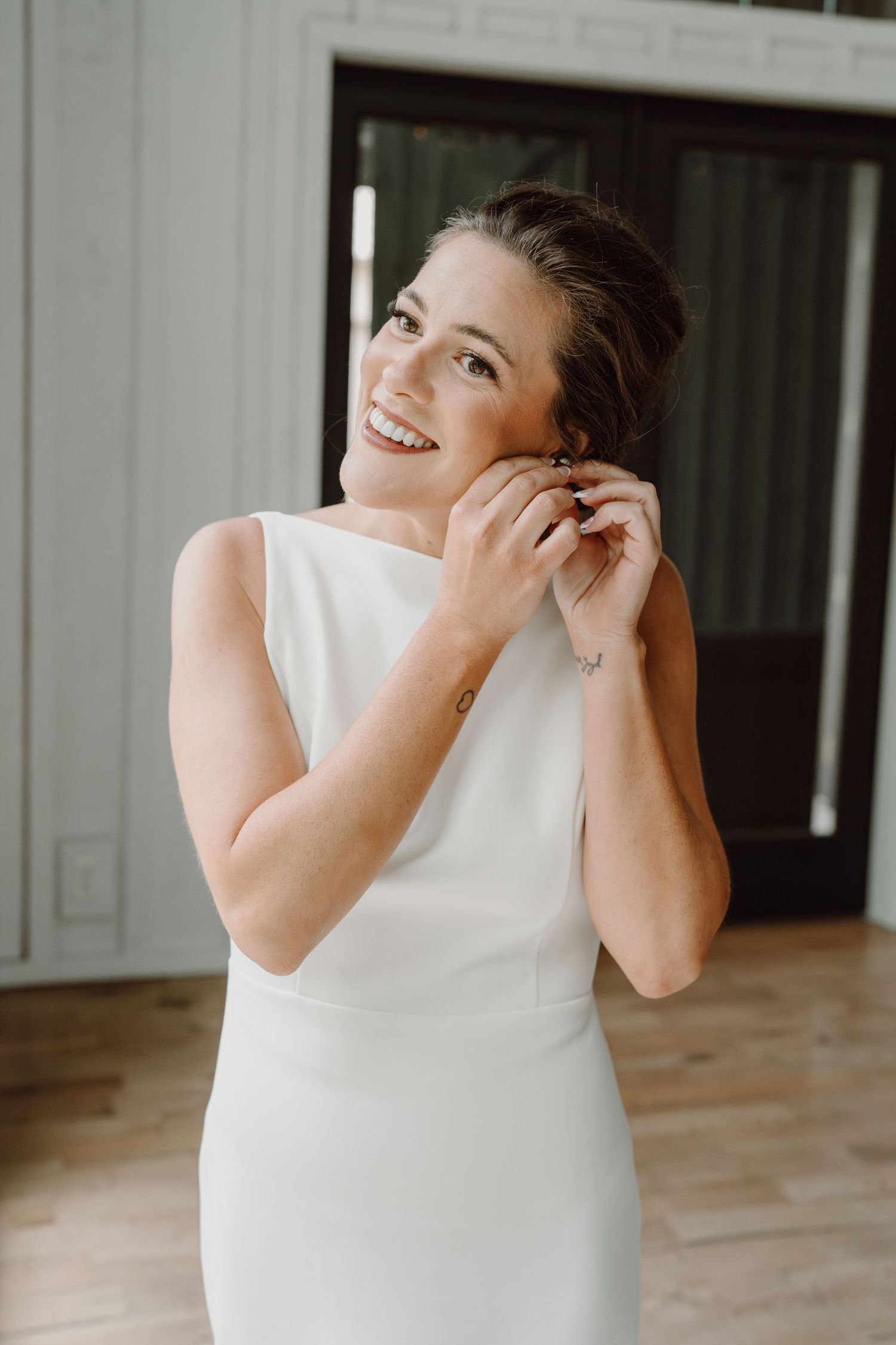 Natural light portrait of someone in a white sleeveless wedding dress touching their earrings.