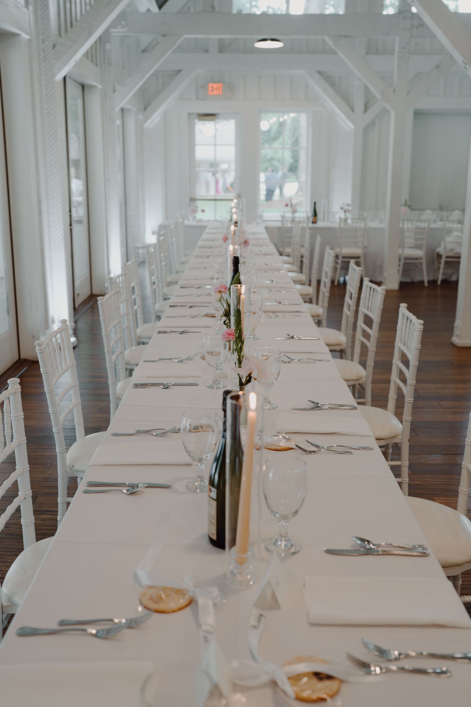 Long white dining table set for a formal event with place settings and wine bottles in an elegant white room.