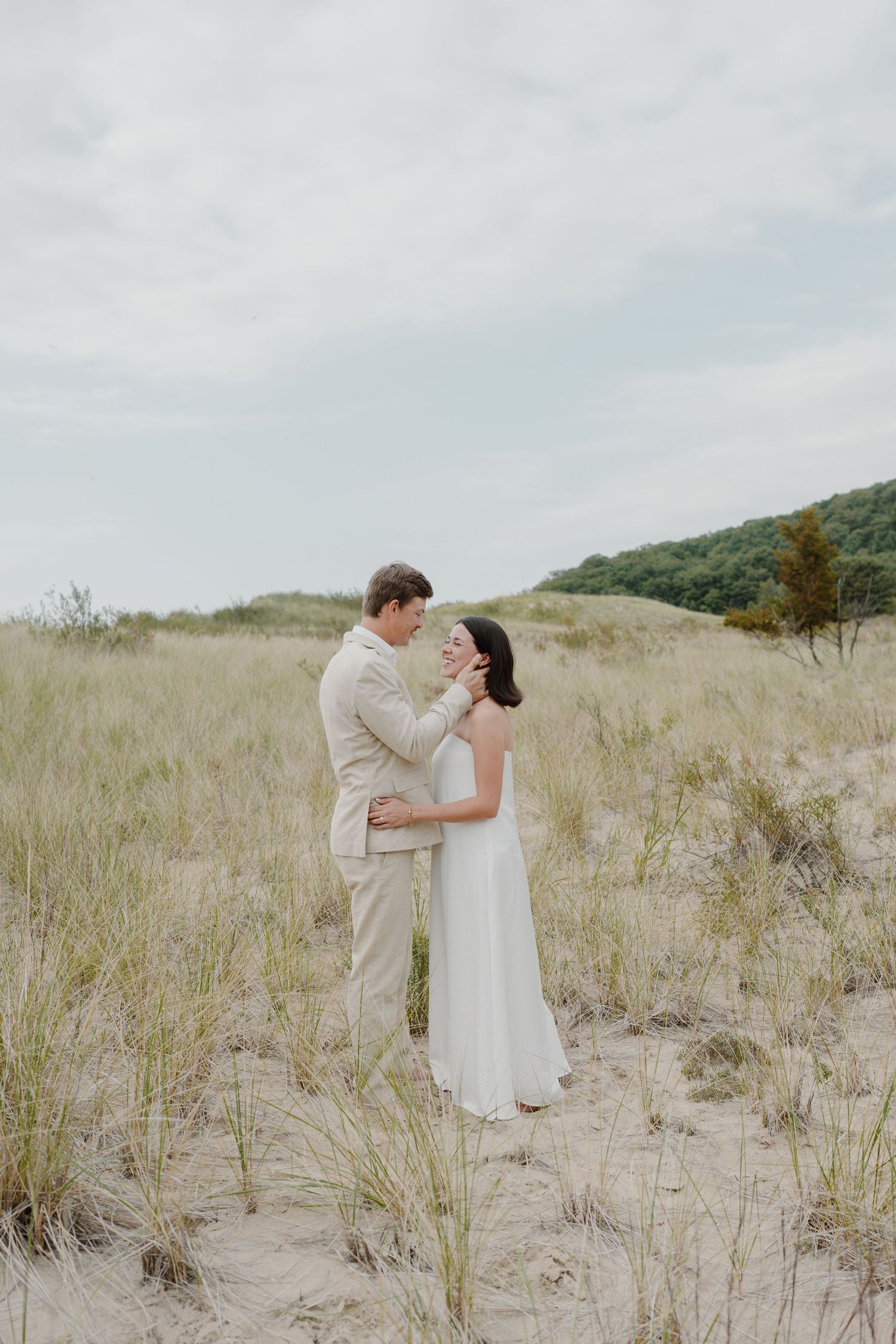 Wedding couple shares romantic moments together on sandy beach dunes under overcast skies.