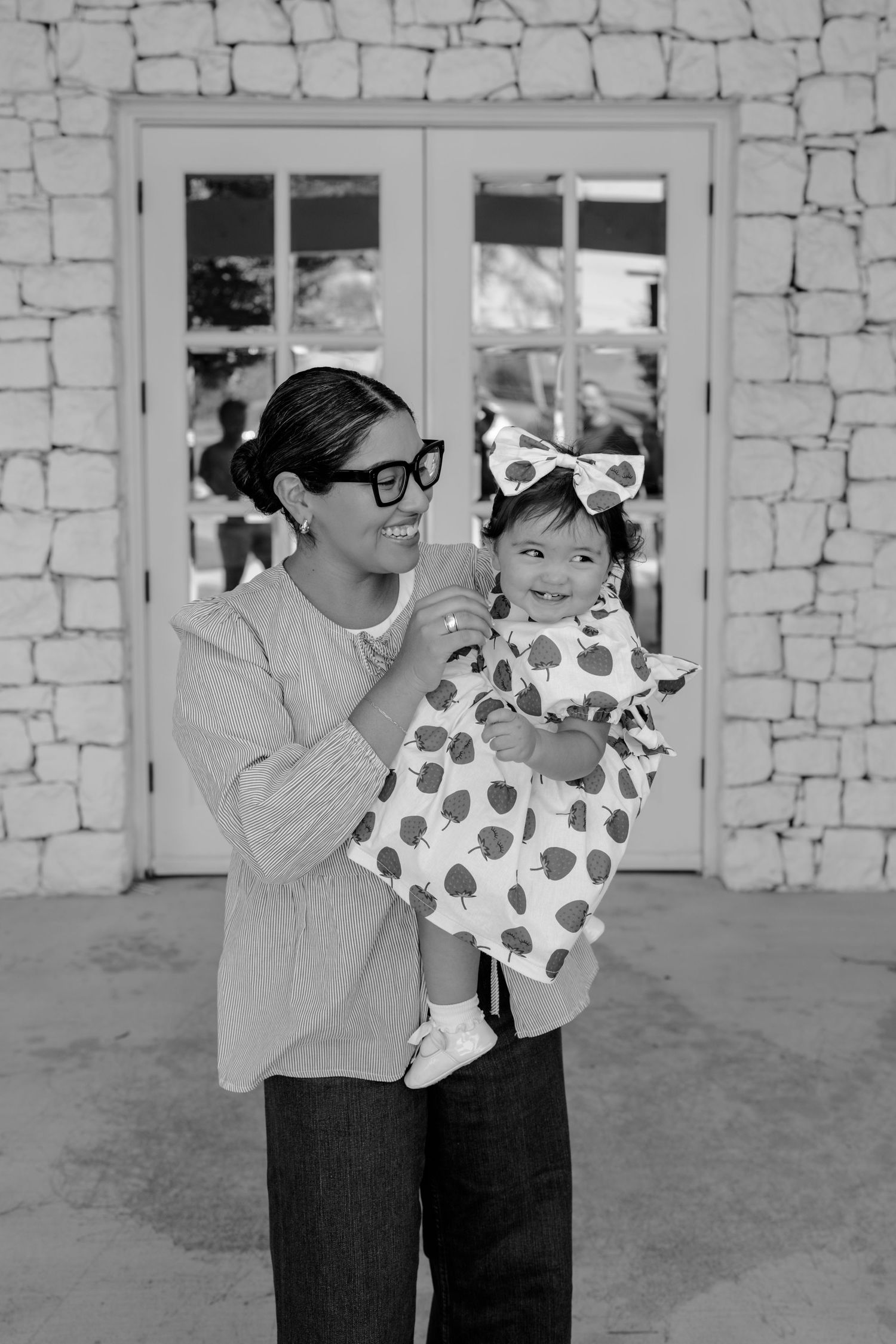 Black and white capture of joyful parent-child moment against textured wall backdrop.