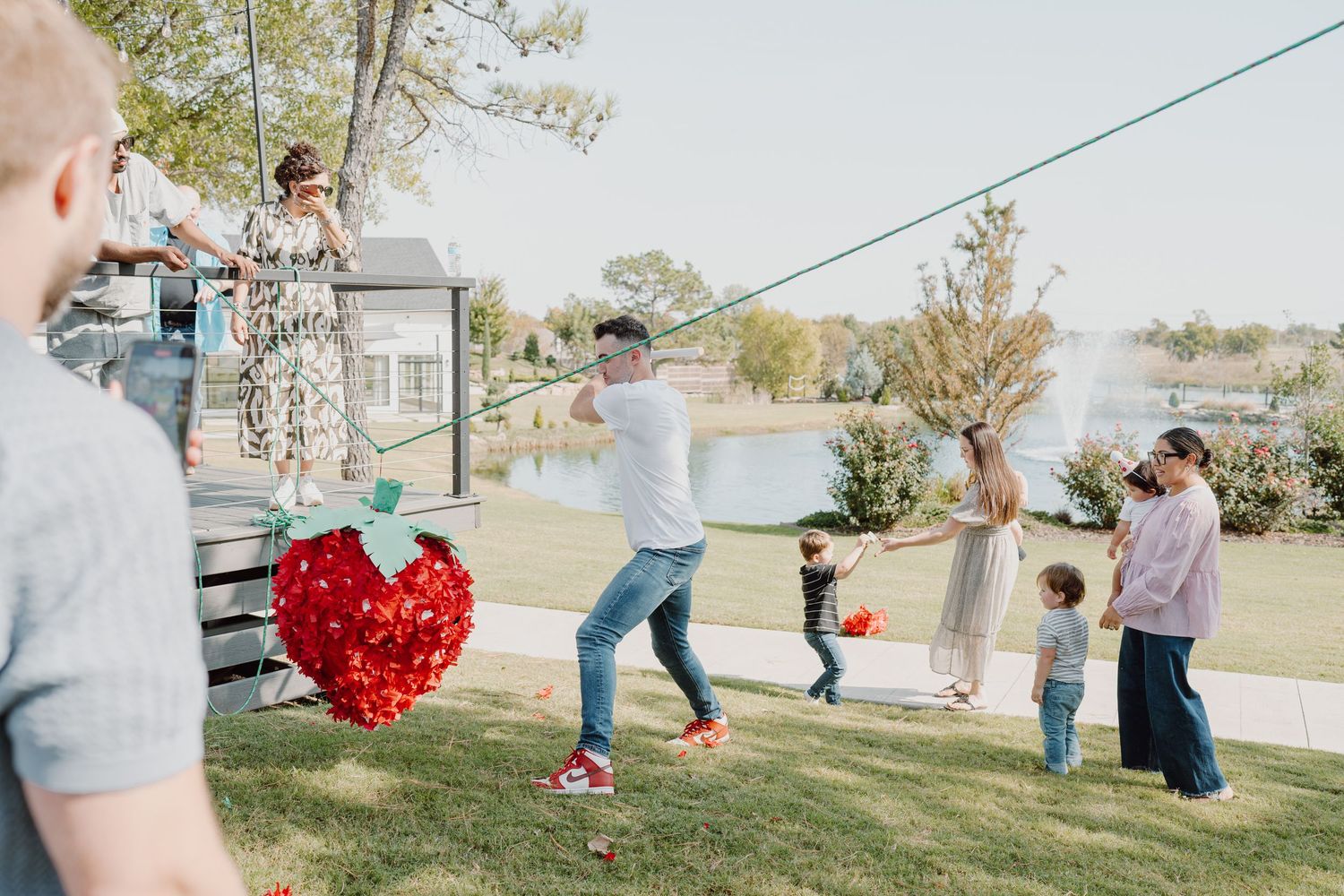 Children playing outdoors and collecting scattered red decorations on a grassy lawn.