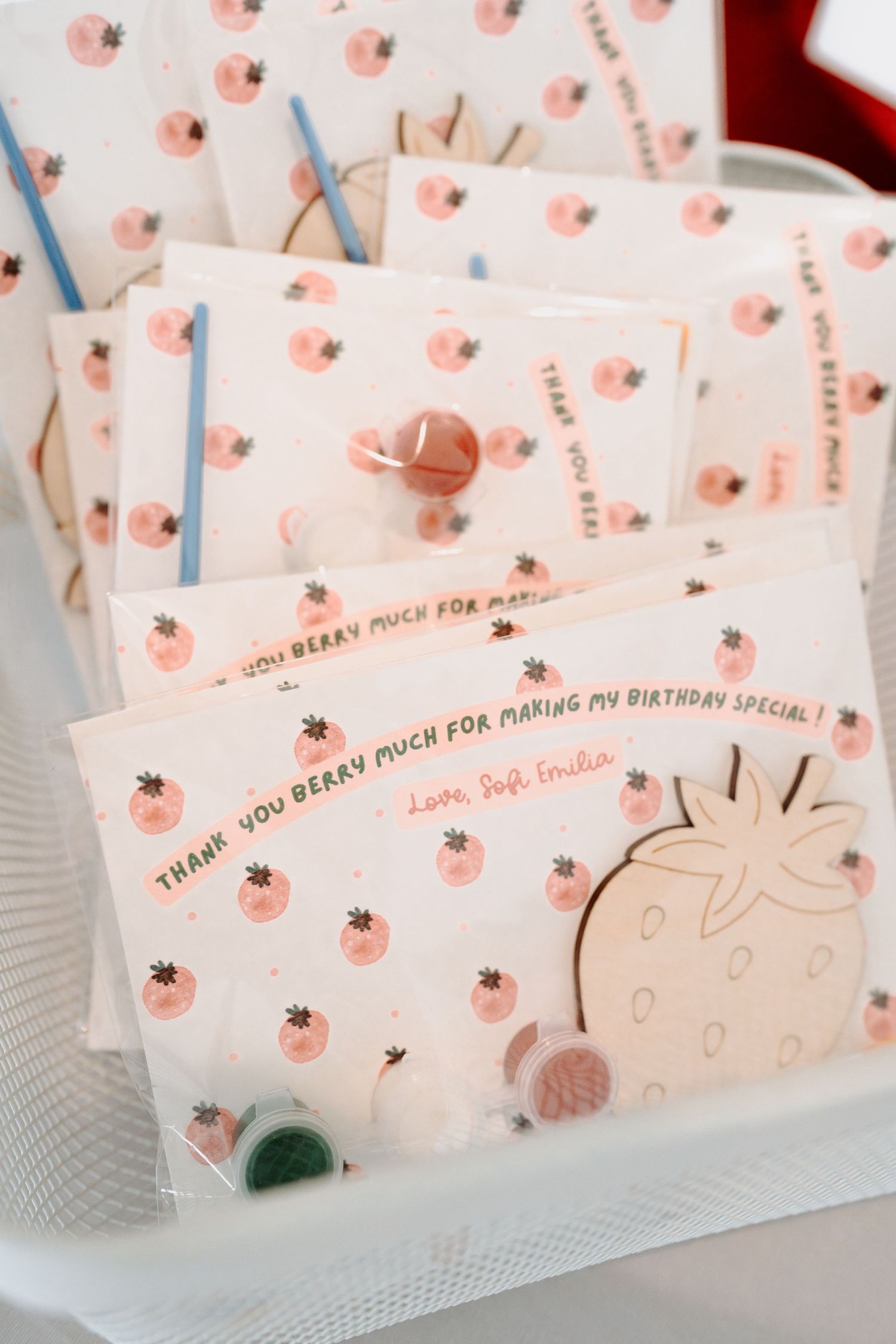 Pink strawberry themed place cards with decorative designs displayed in a row for a birthday celebration.