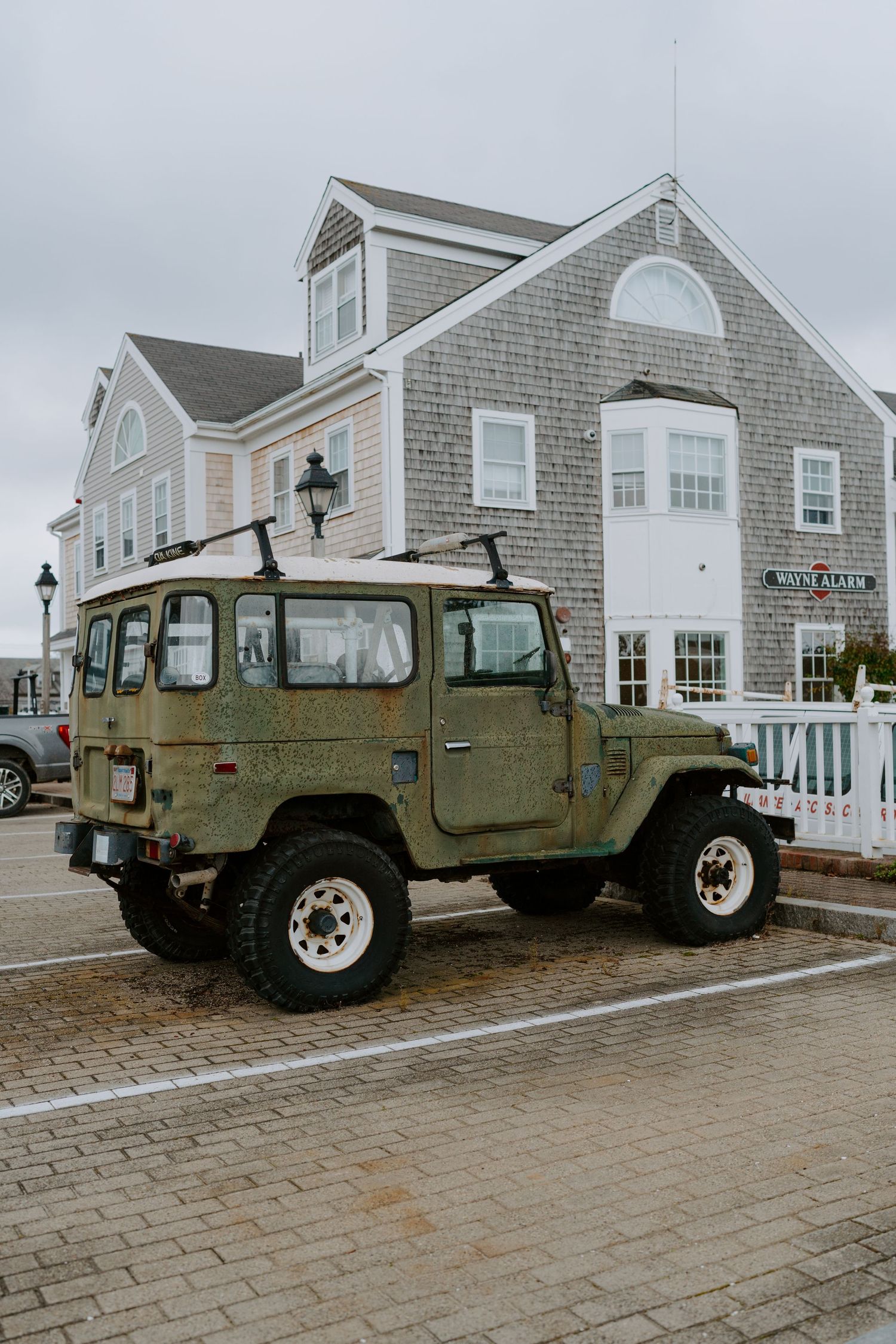 Row of military-style Humvee vehicles parked in front of grey shingled coastal homes.
