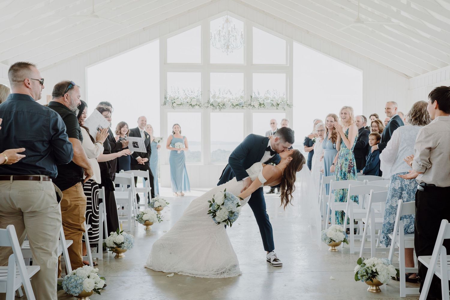 Bright white indoor reception space filled with wedding guests celebrating during a dance party.