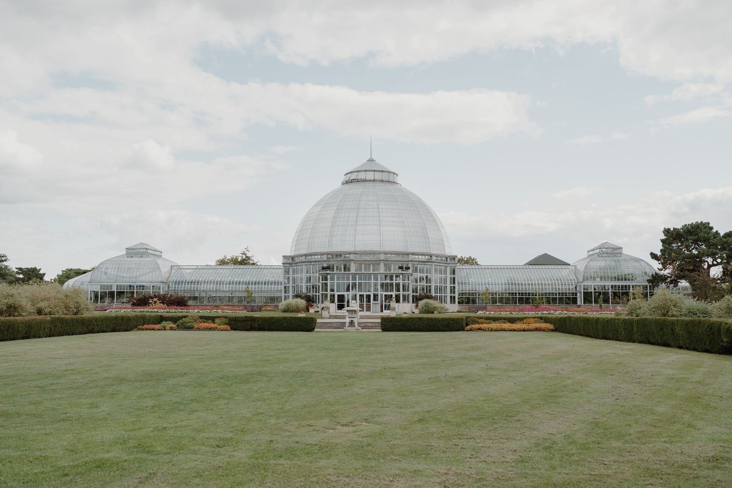 Panoramic view of a glass conservatory building with a domed roof against a cloudy sky.