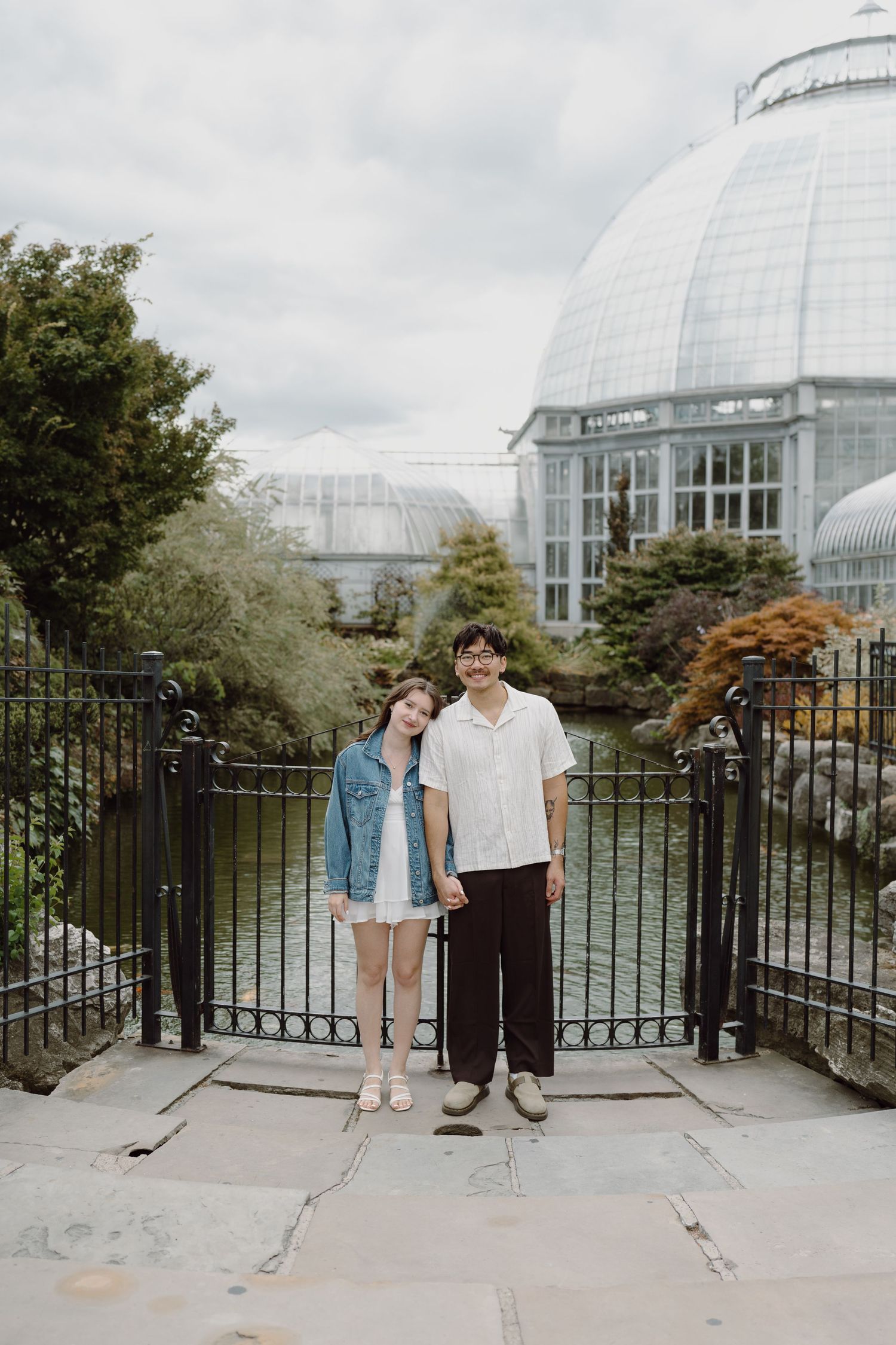 Couple standing on stone path in front of glass conservatory dome and garden.