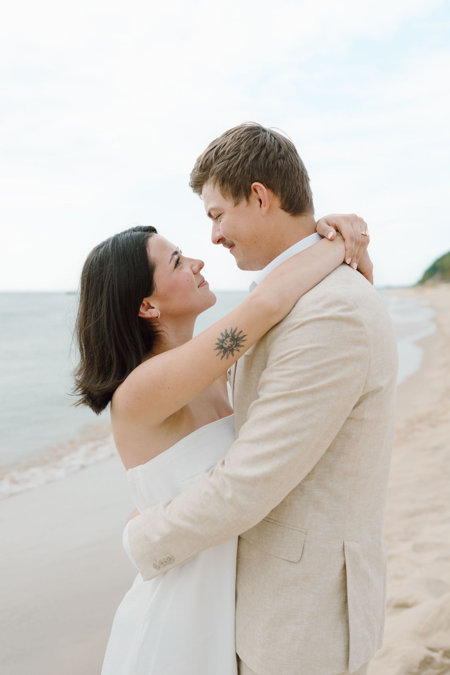 Couple in coordinated outfits share intimate moment against bright beach backdrop.