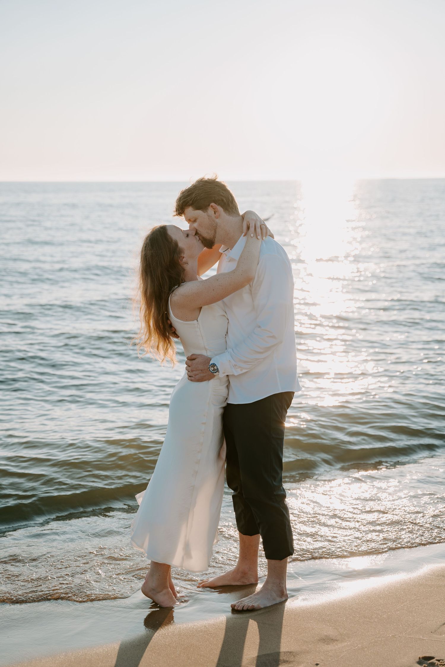 Romantic couple embracing on beach at sunset with ocean waves in background.