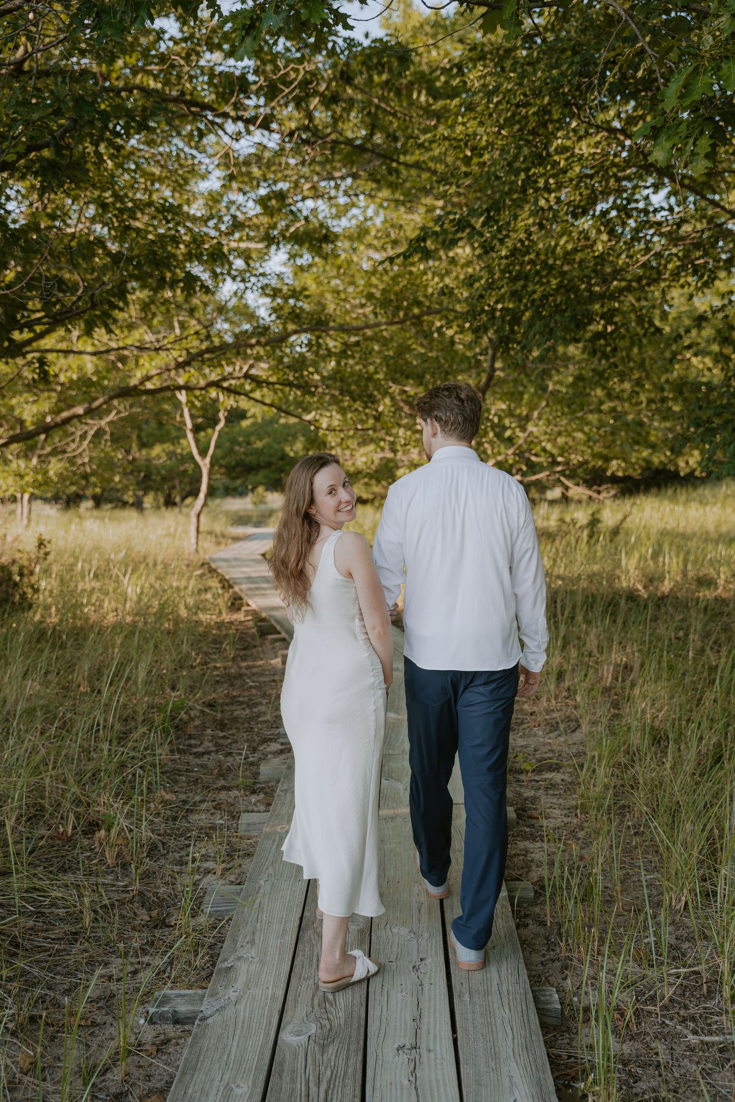 A couple strolls hand in hand along a wooden boardwalk surrounded by autumn foliage.