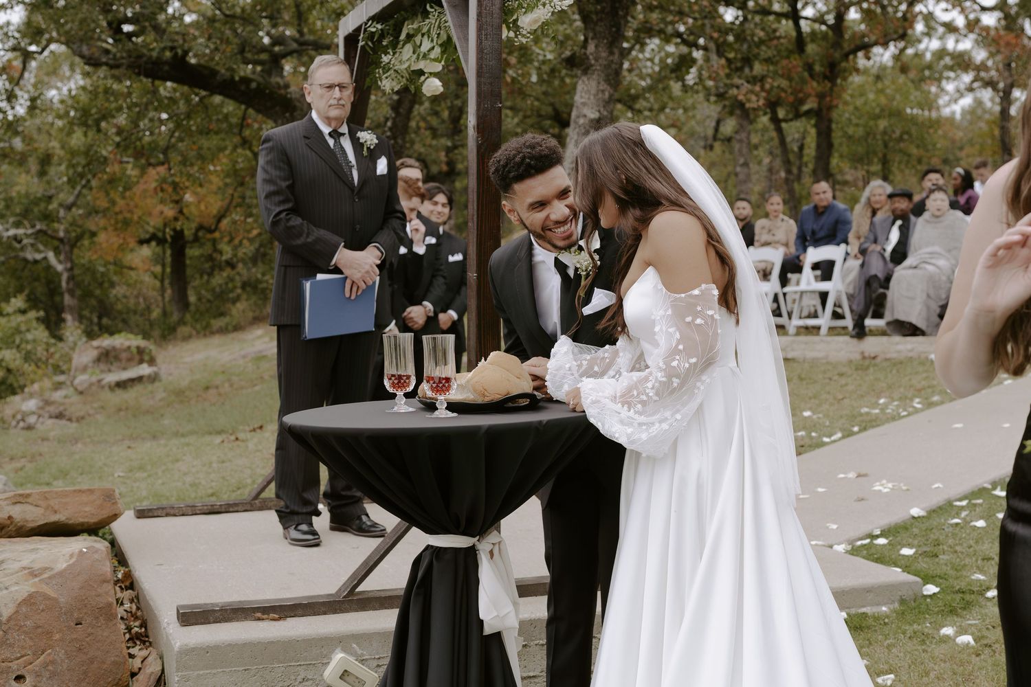 Outdoor wedding ceremony with wooden arch decorated with white flowers overlooking mountain landscape.