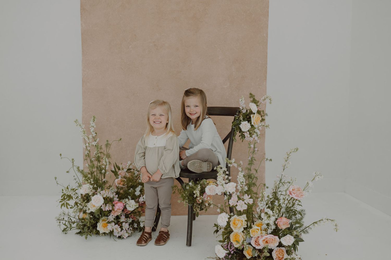Minimalist studio setup with fresh flower arrangements and vintage chair against neutral wall.